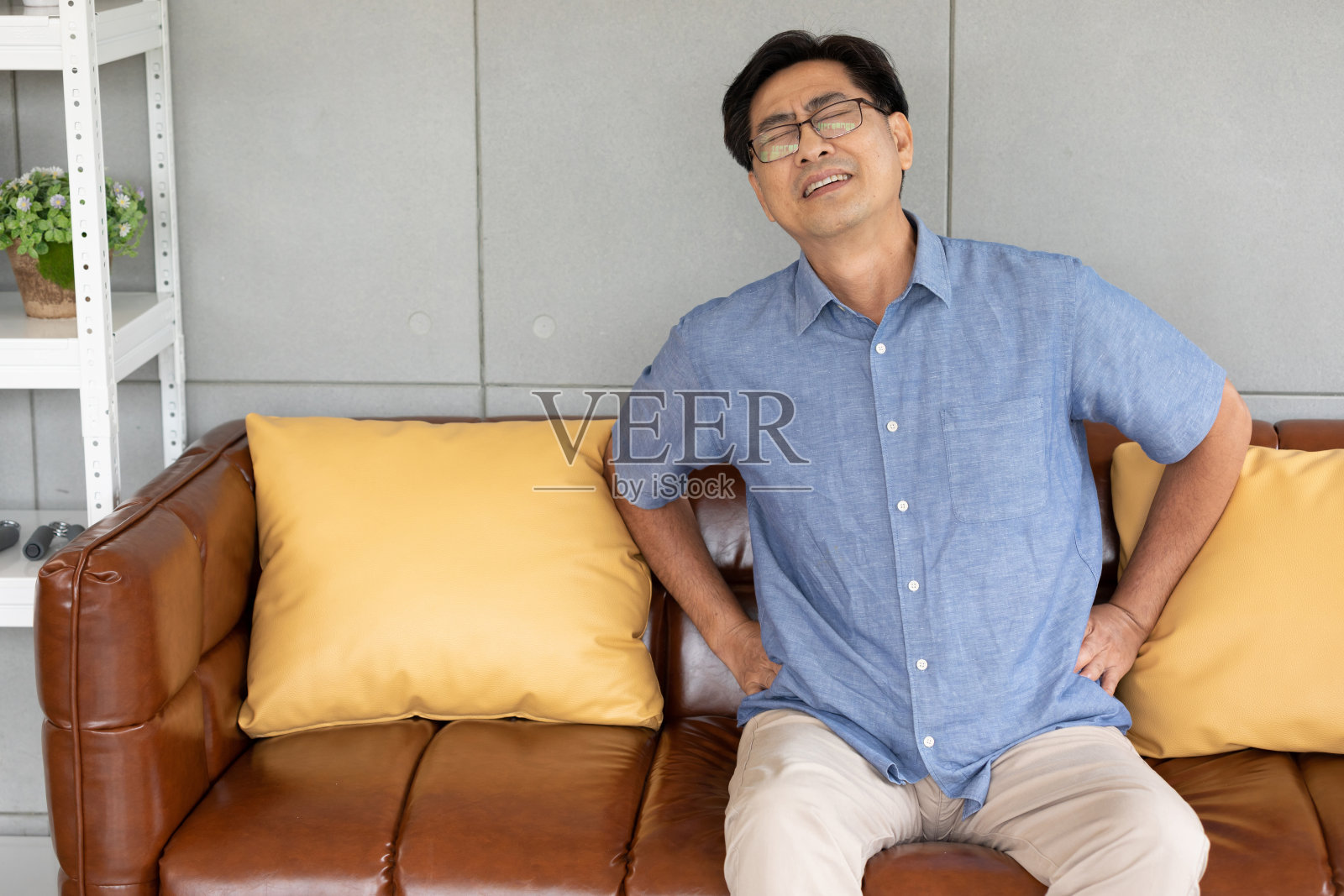 年长的亚洲男人在家里遭受背部和腰部的疼痛照片摄影图片