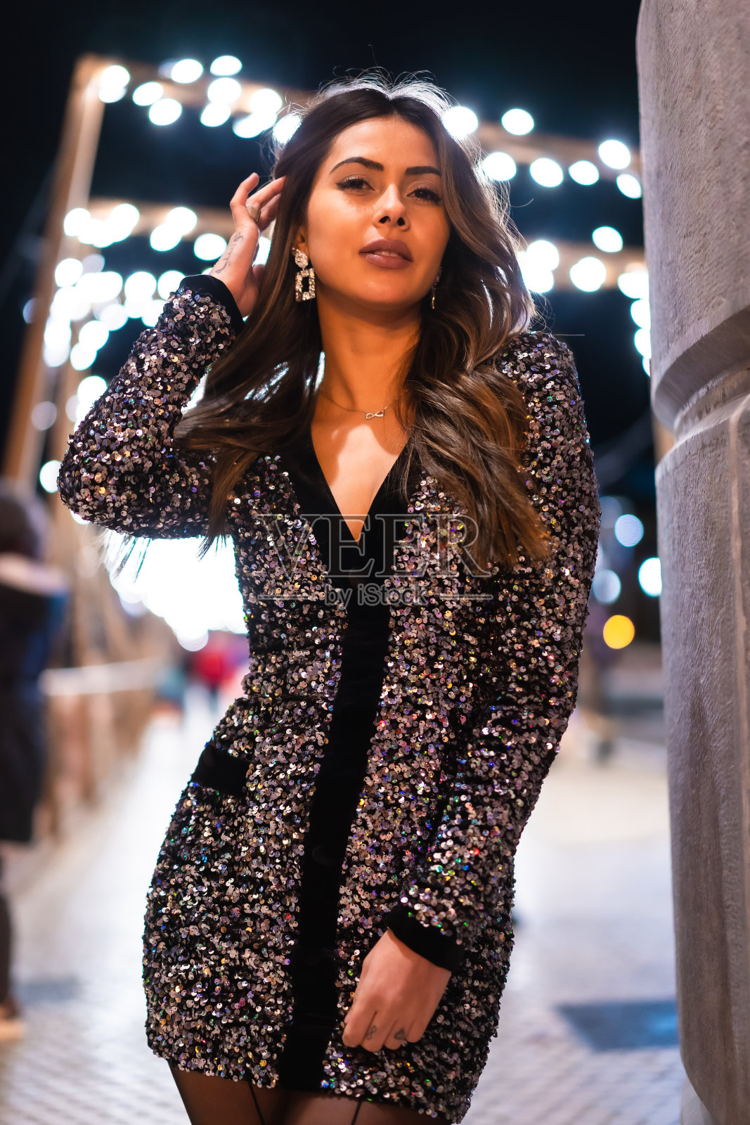 圣诞节的生活方式。深色头发的白人模特穿着时尚的亮片连衣裙,肖像在城市圣诞灯光照片摄影图片