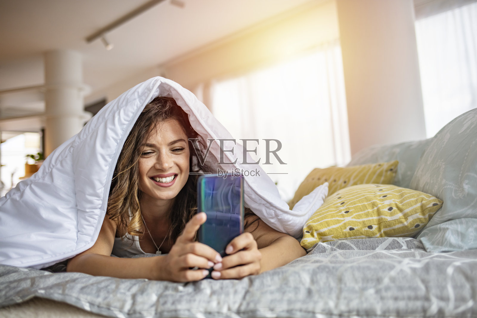 女人躺在床上拿着智能手机大笑。照片摄影图片