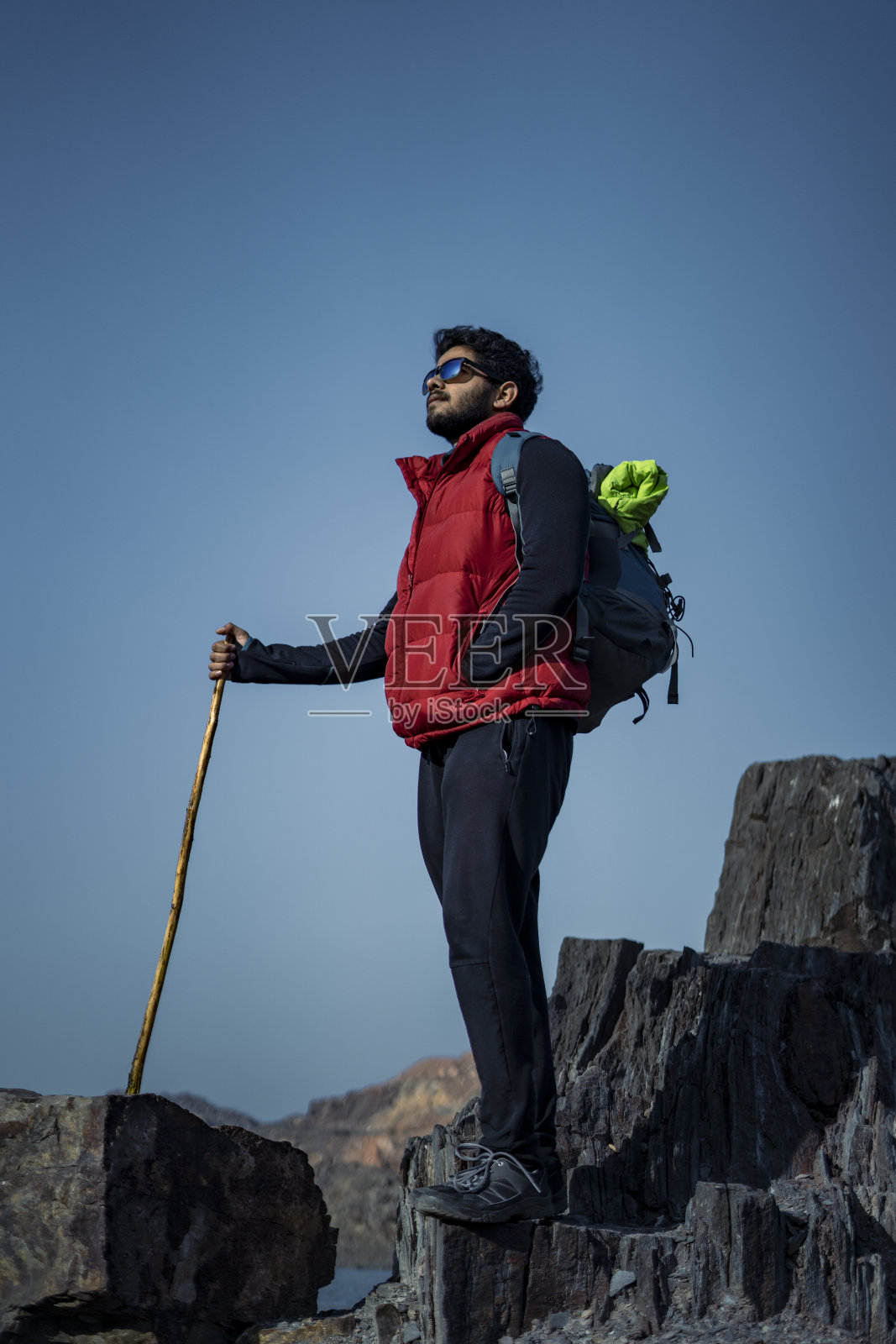 年轻的印度旅行者背着背包和一根棍子爬山,背景是美丽的湖景。运动和自由的概念。照片摄影图片