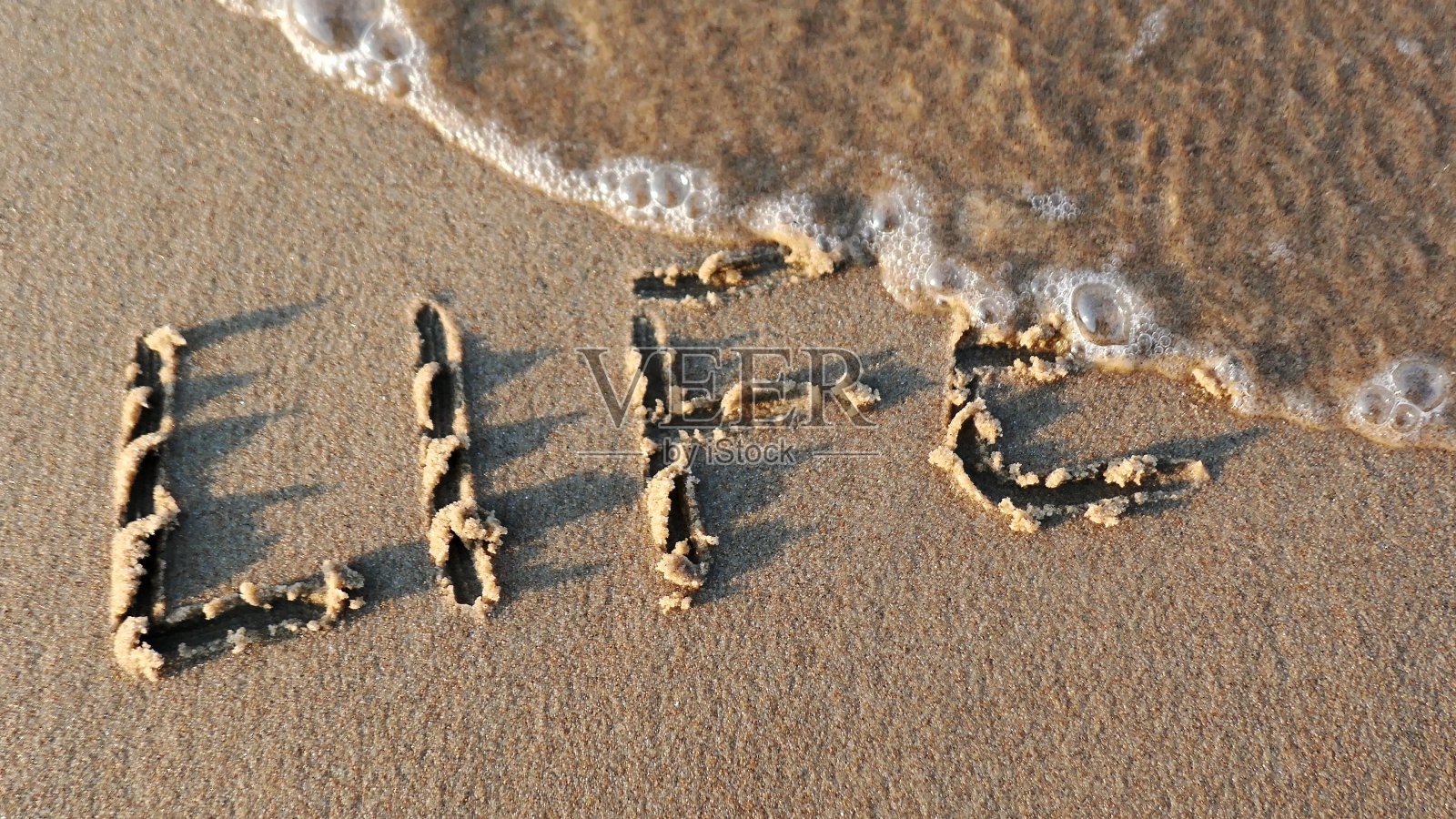 沙滩上手写的“生活”字样被日落时分的海浪抹去照片摄影图片