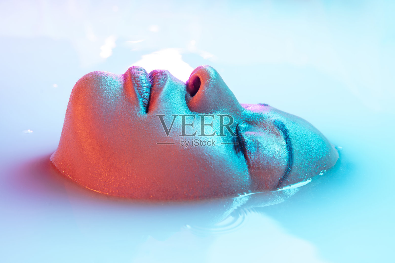 美丽女性的脸在牛奶浴中柔和地泛着蓝粉色的霓虹灯照片摄影图片