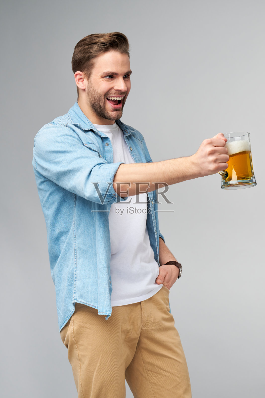 年轻人拿着穿着牛仔裤衬衫拿着一杯啤酒站在灰色背景照片摄影图片