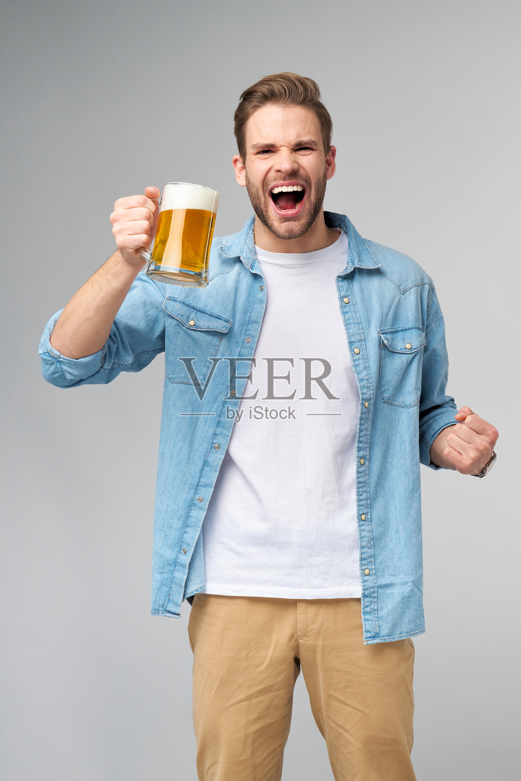 年轻人拿着穿着牛仔裤衬衫拿着一杯啤酒站在灰色背景照片摄影图片