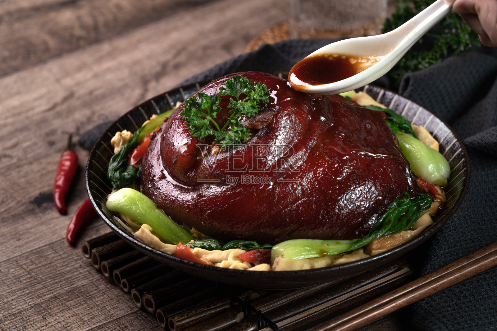 用勺子把可口的酱油倒在盘子里的台湾红烧猪腿上。照片摄影图片