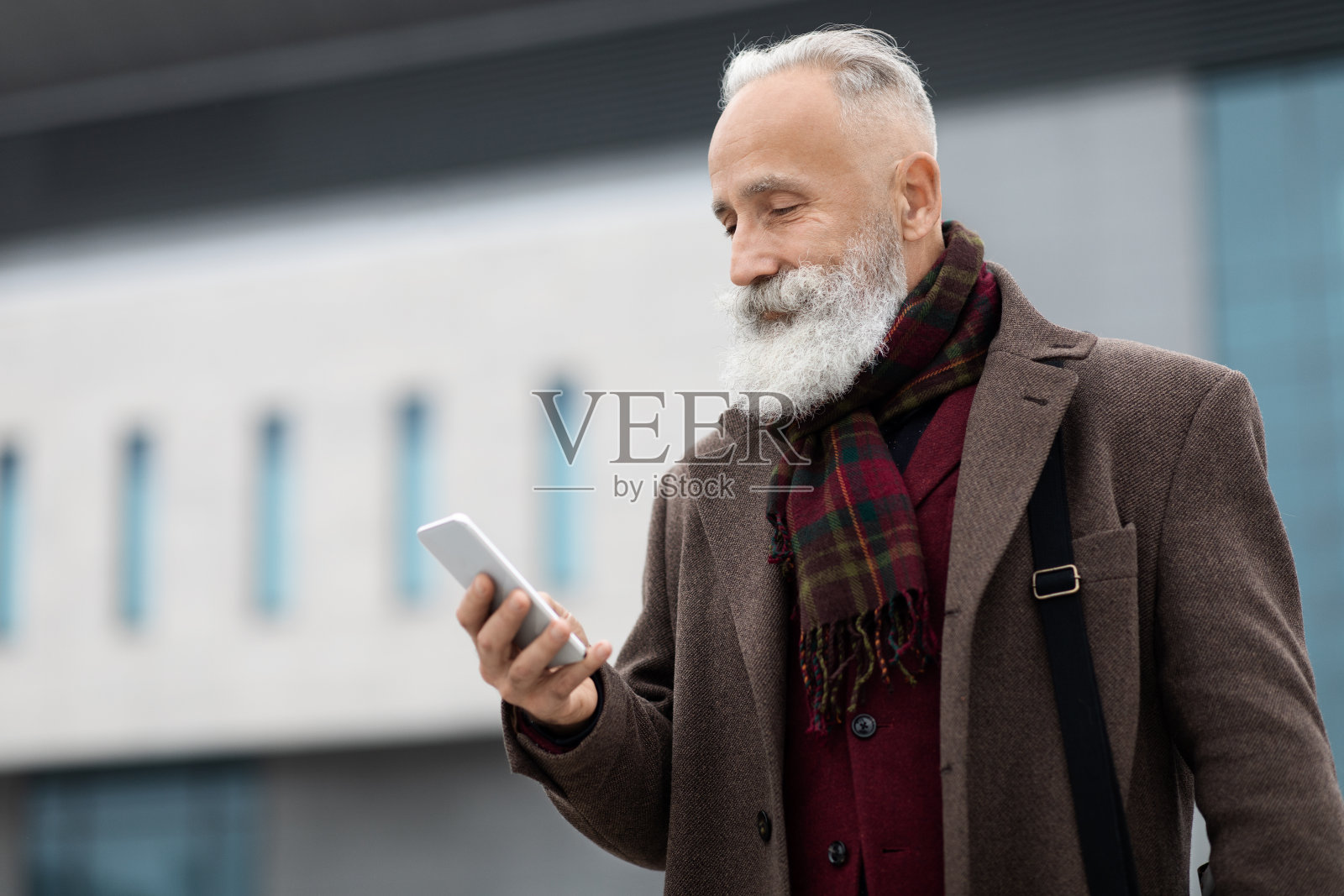 头发花白的商人下班回家,看着智能手机的屏幕照片摄影图片