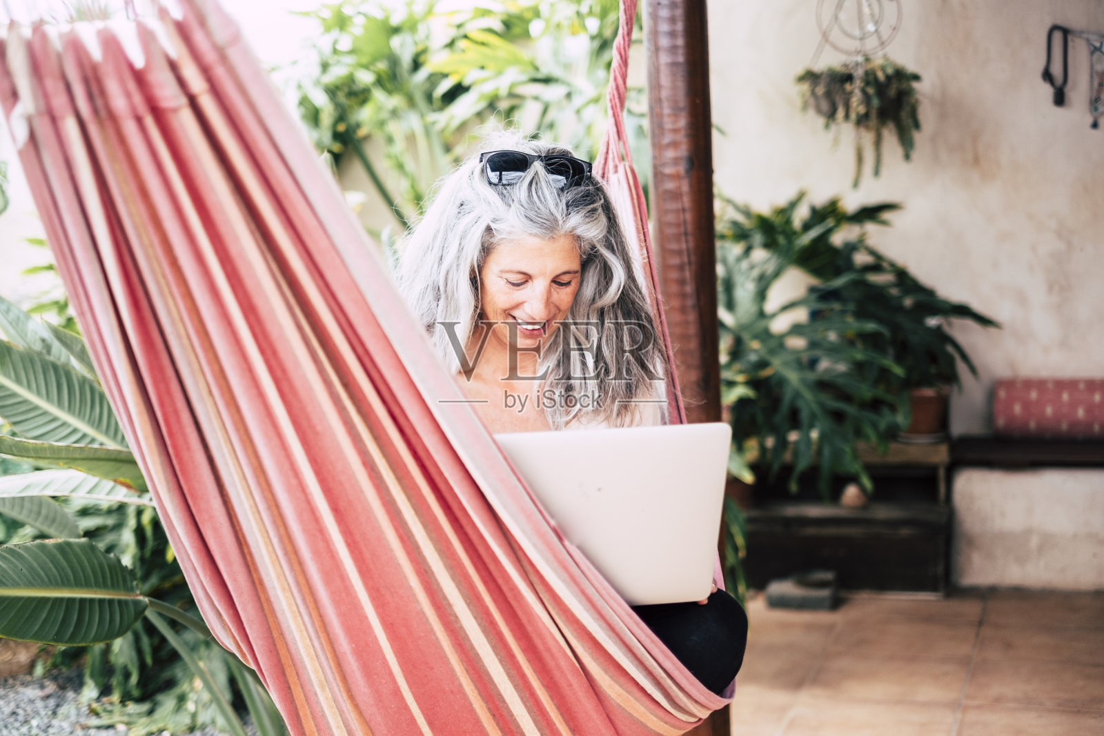 成年中年白人妇女在家工作坐在花园里的吊床上-技术在线的概念,人们连接和智能工作-现代女性和电脑照片摄影图片