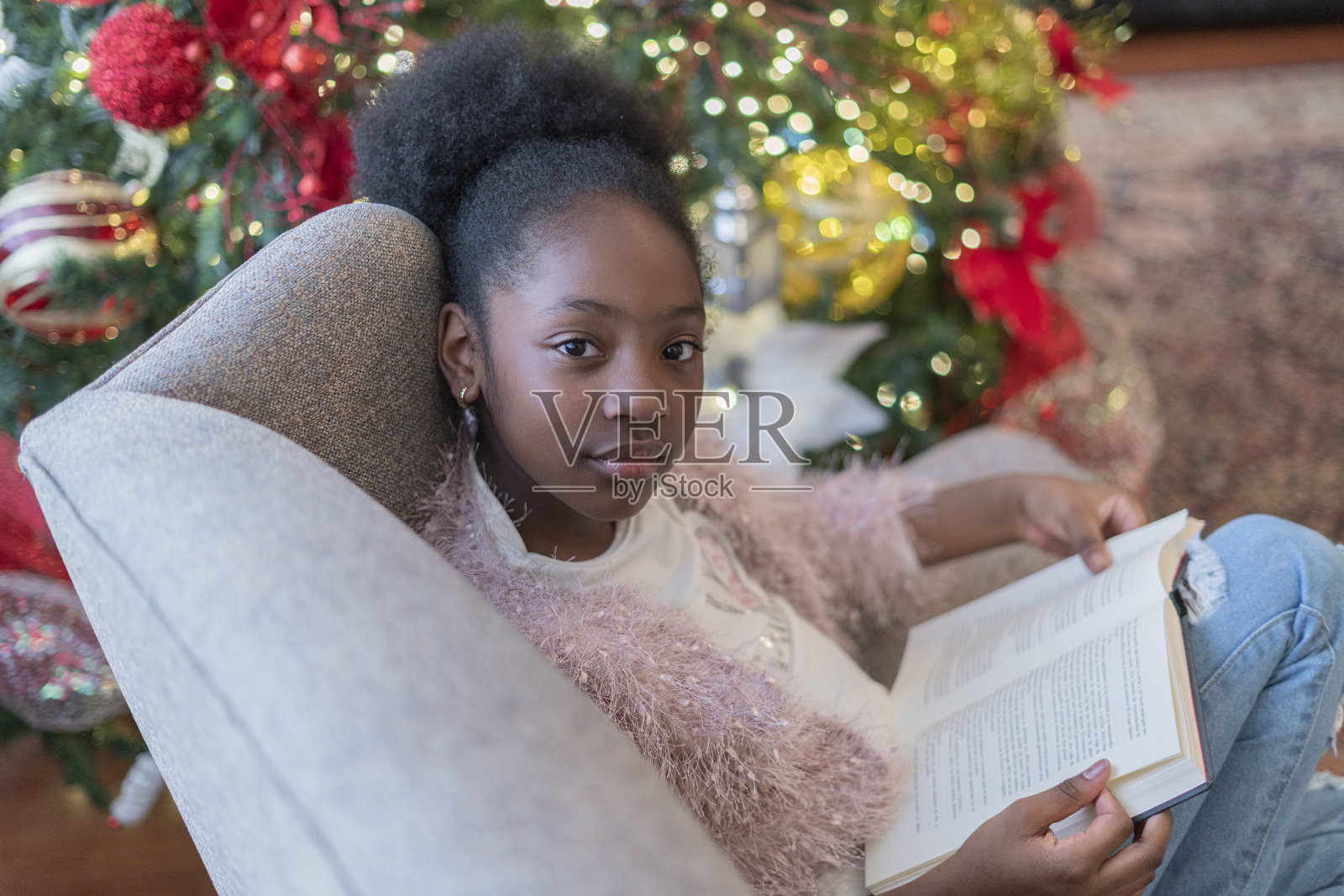 一个长着非洲发式的拉丁女孩正坐在她家的沙发上,手里拿着一本书,微笑着看着相机照片摄影图片