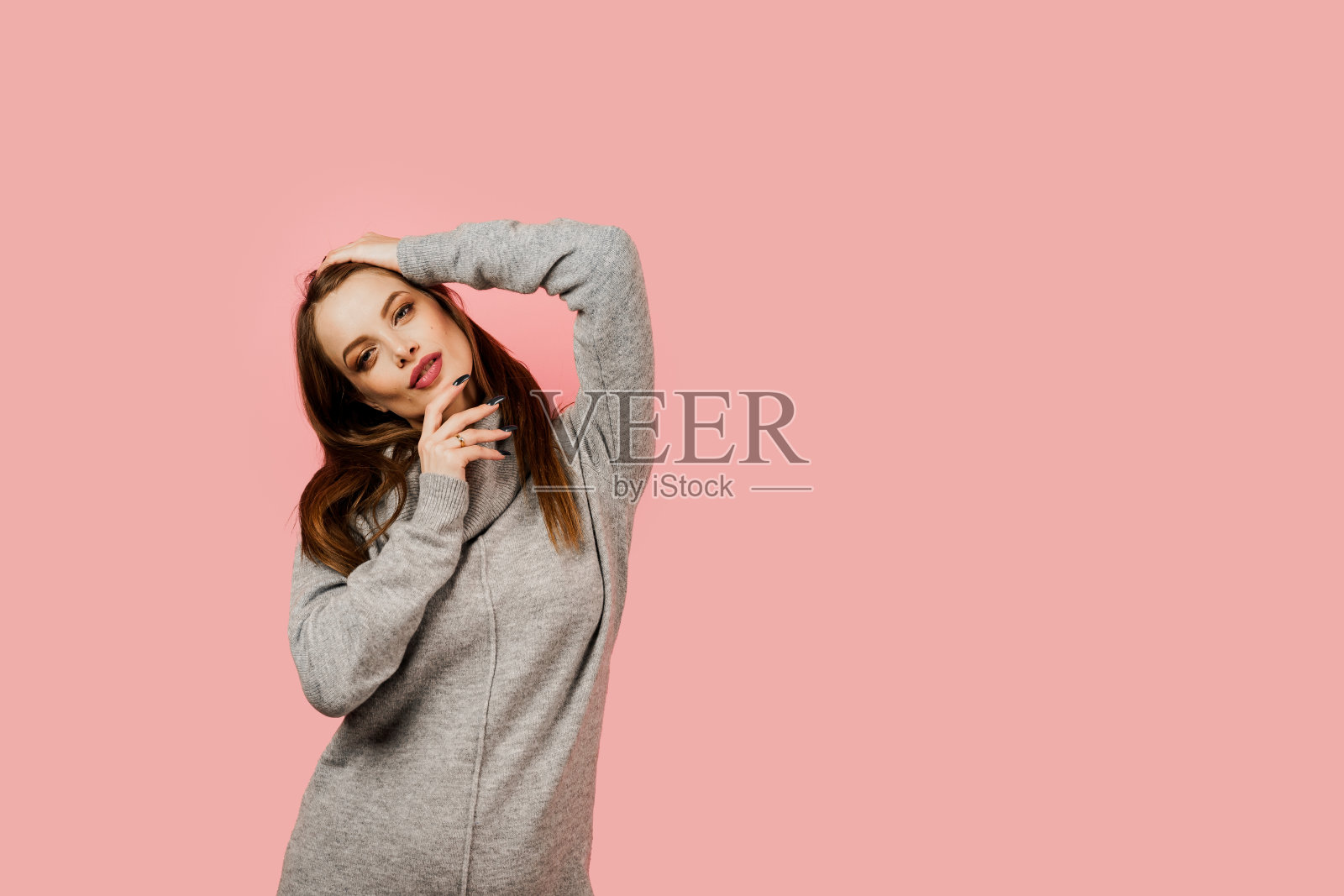 一个穿着灰色毛衣粉红色背景的快乐美丽的女孩怀孕了。怀孕的女人。对孩子的期望。产假。照片摄影图片