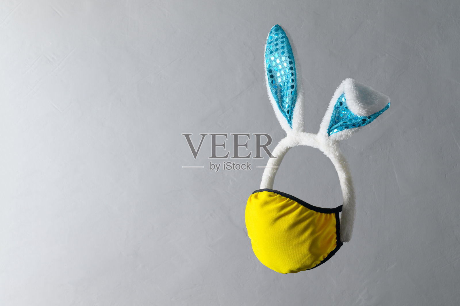 新常态的复活节节日概念。青色兔耳头带和黄色防护面罩,灰色背景的创意悬浮构图。飞行物体,拷贝空间照片摄影图片