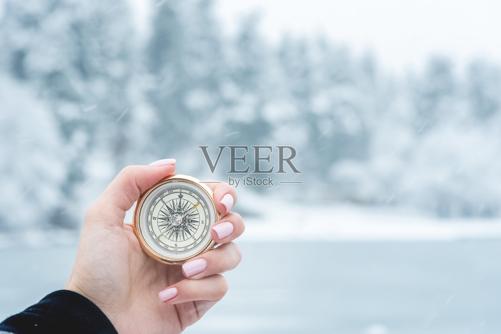 第一人称视角的女性手与指南针在一个冬天的森林和冰冻的湖的背景。导航的概念,寻找自己的路径和方向的基本点照片摄影图片