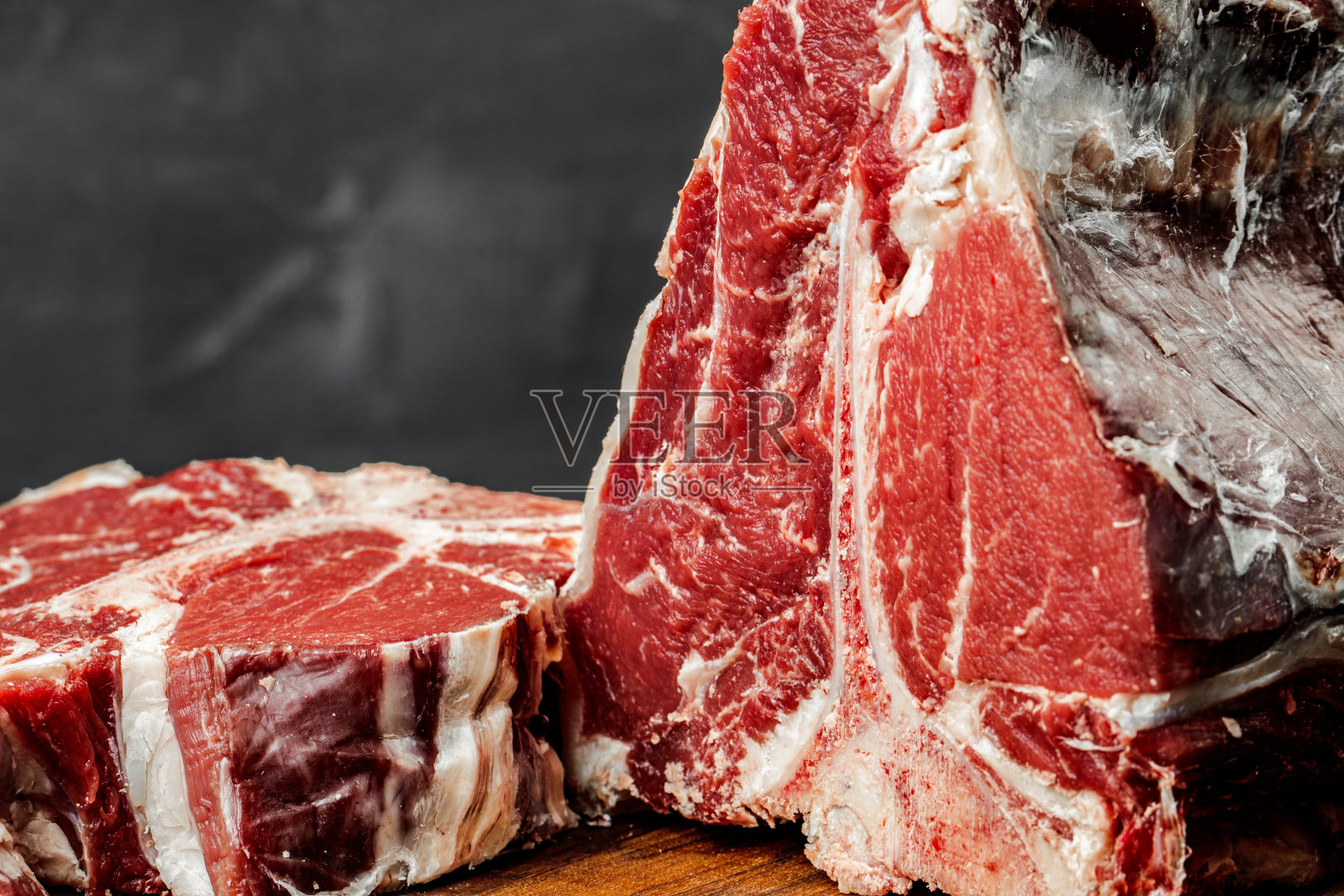 生的t骨牛排在石黑色的桌子上烹饪。照片摄影图片