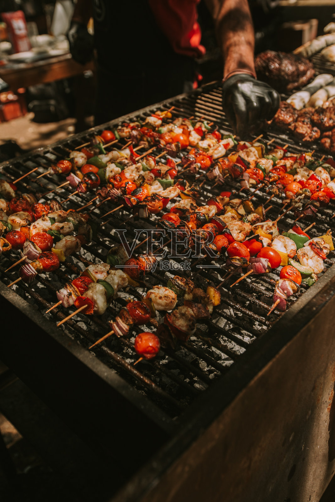 黑手套厨师烹饪虾串和烤蔬菜。照片摄影图片