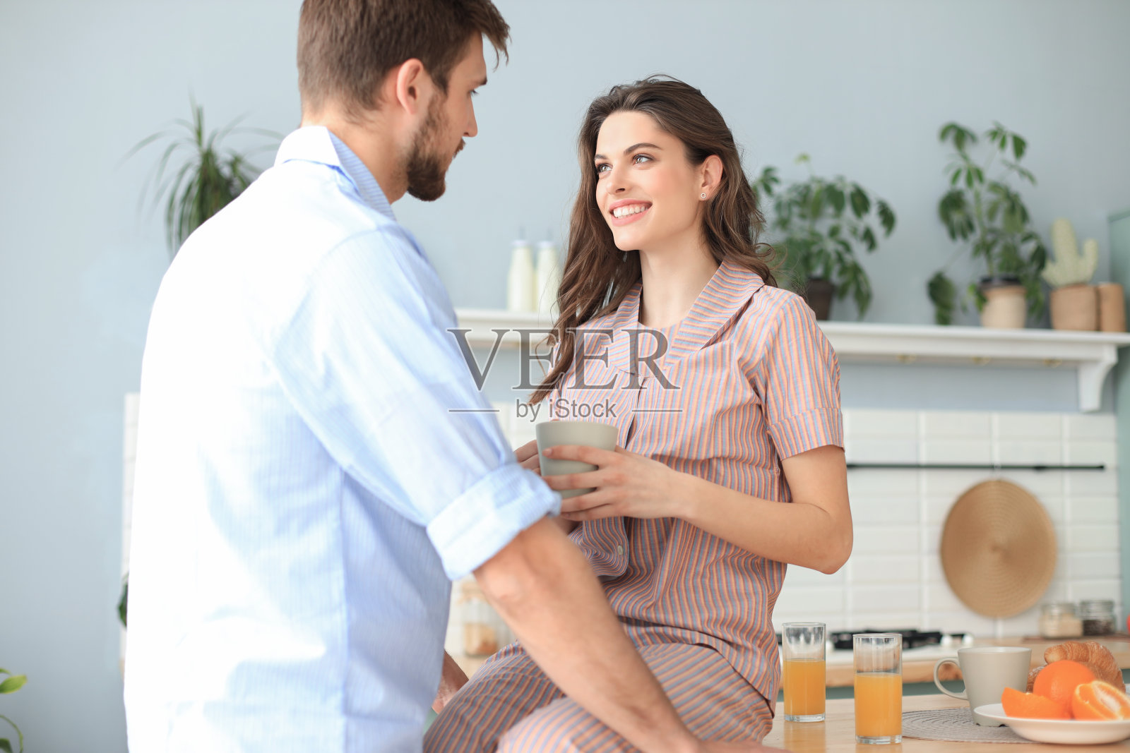 一对漂亮的年轻夫妇穿着睡衣看着对方,微笑着在厨房做饭。照片摄影图片