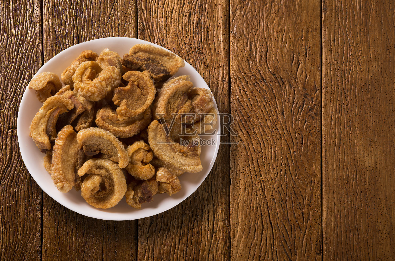 一堆炸熏肉块在一个白色的盘子在木头背景。照片摄影图片