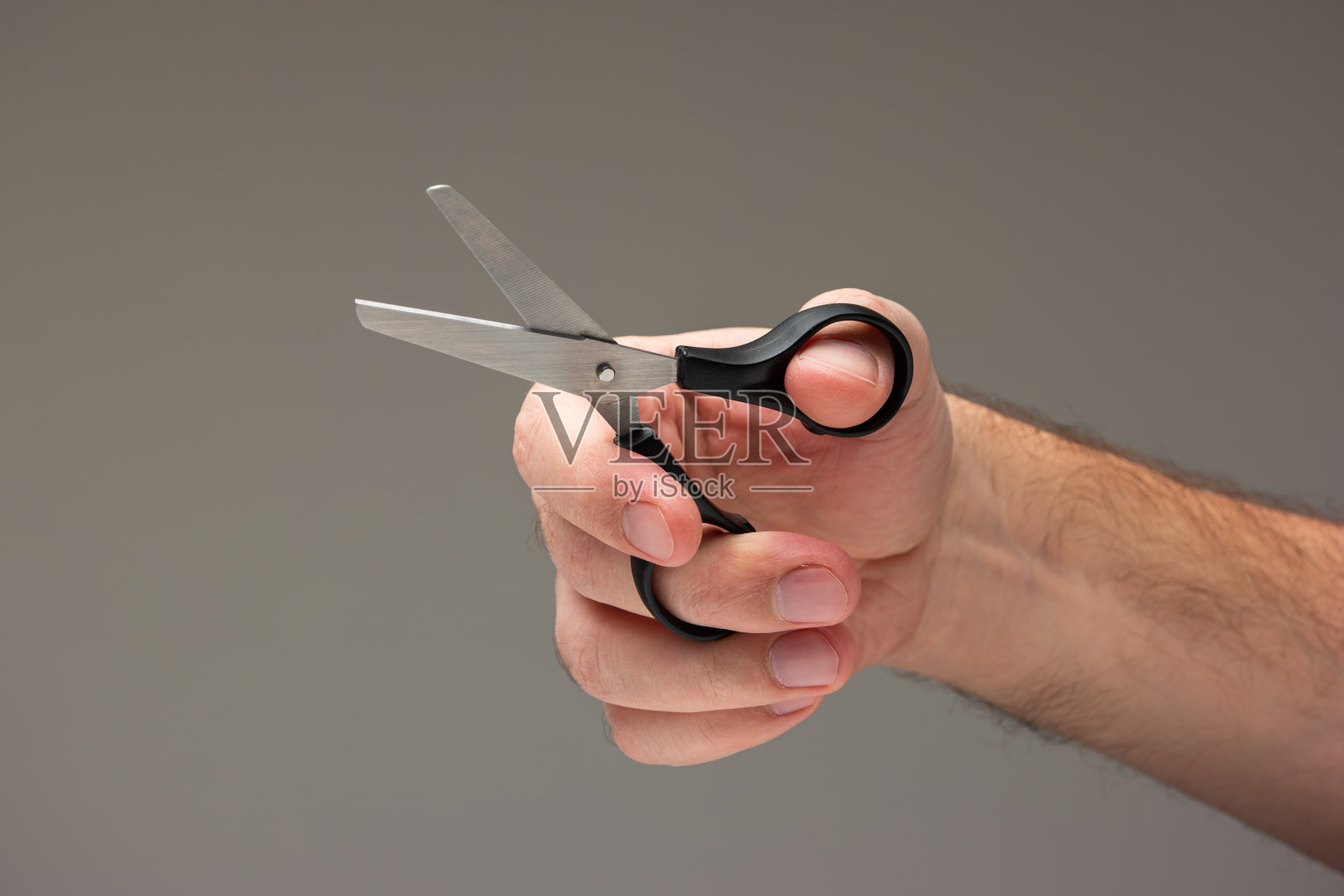 白人男性的手拿着一个小工艺剪刀与黑色塑料处理孤立在灰色背景照片摄影图片