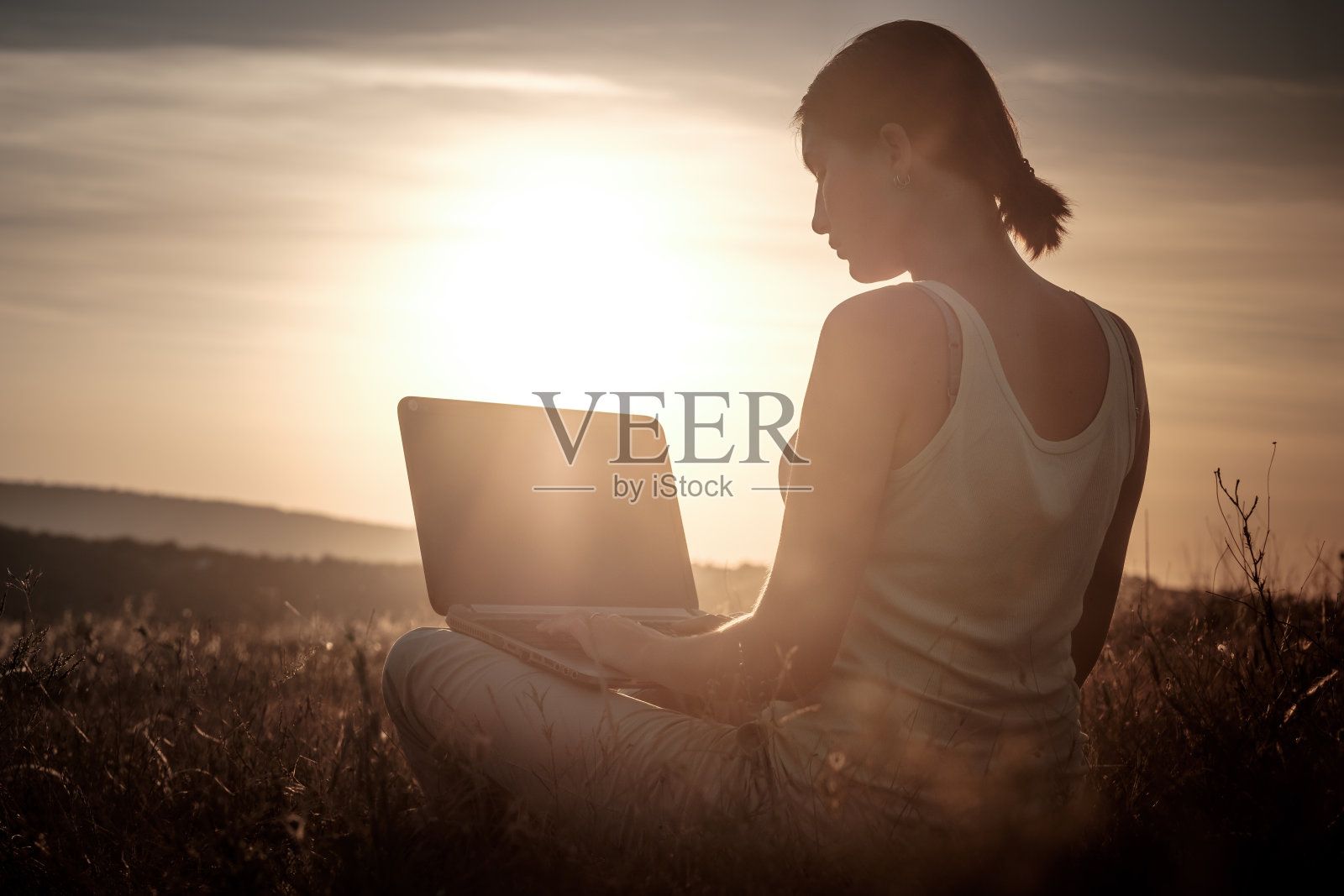 一个女孩的剪影与笔记本电脑在日落或日出的背景照片摄影图片