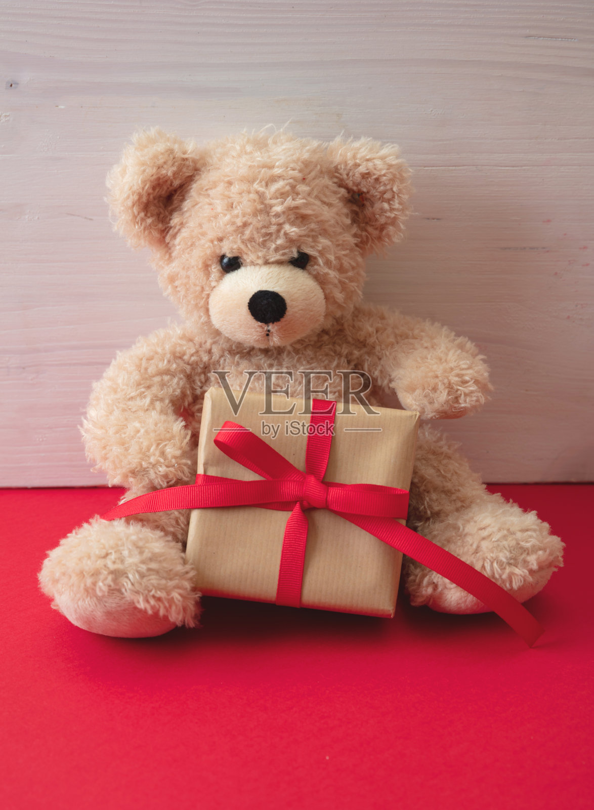 泰迪熊拿着礼盒坐在红色的地板上。情人节。照片摄影图片