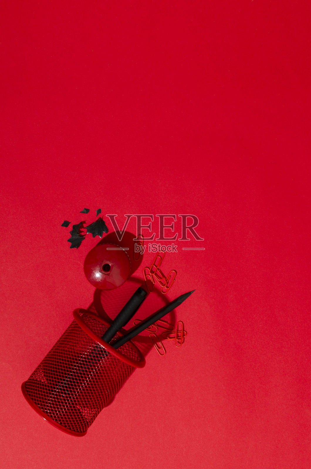 顶视图的笔筒,铅笔,钢笔,卷笔刀,钢笔刨花上的红色背景。空的空间照片摄影图片