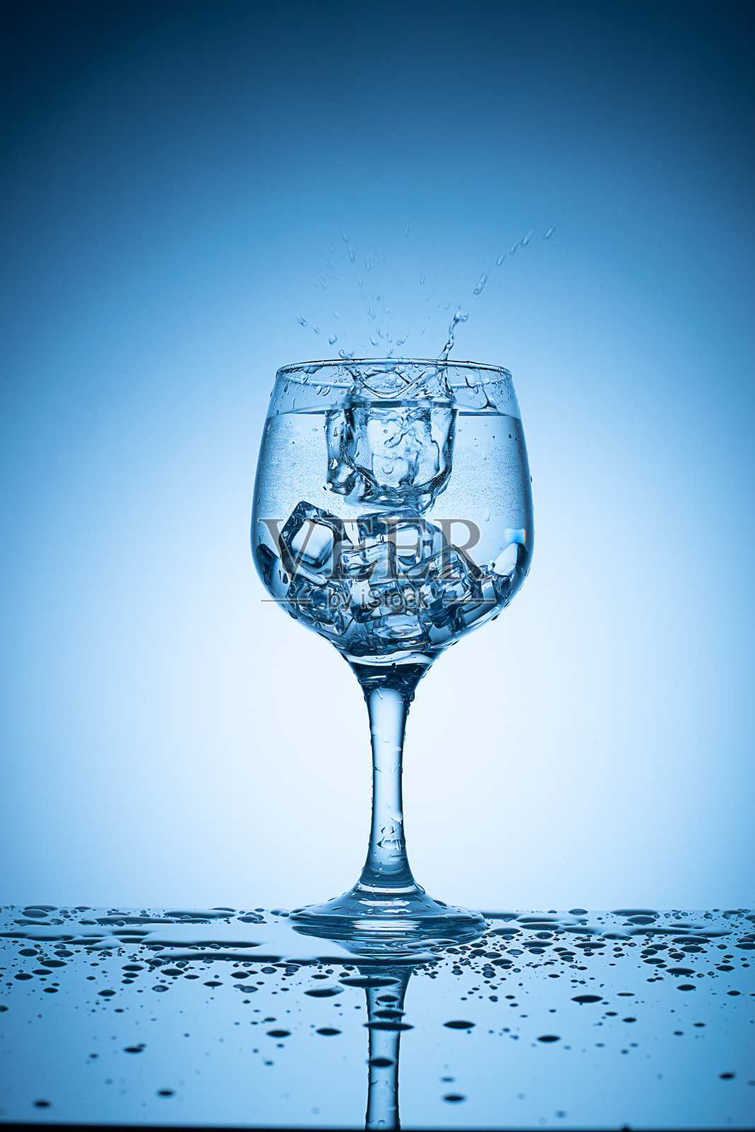 冰块倒入鸡尾酒杯,溅起水花。照片摄影图片