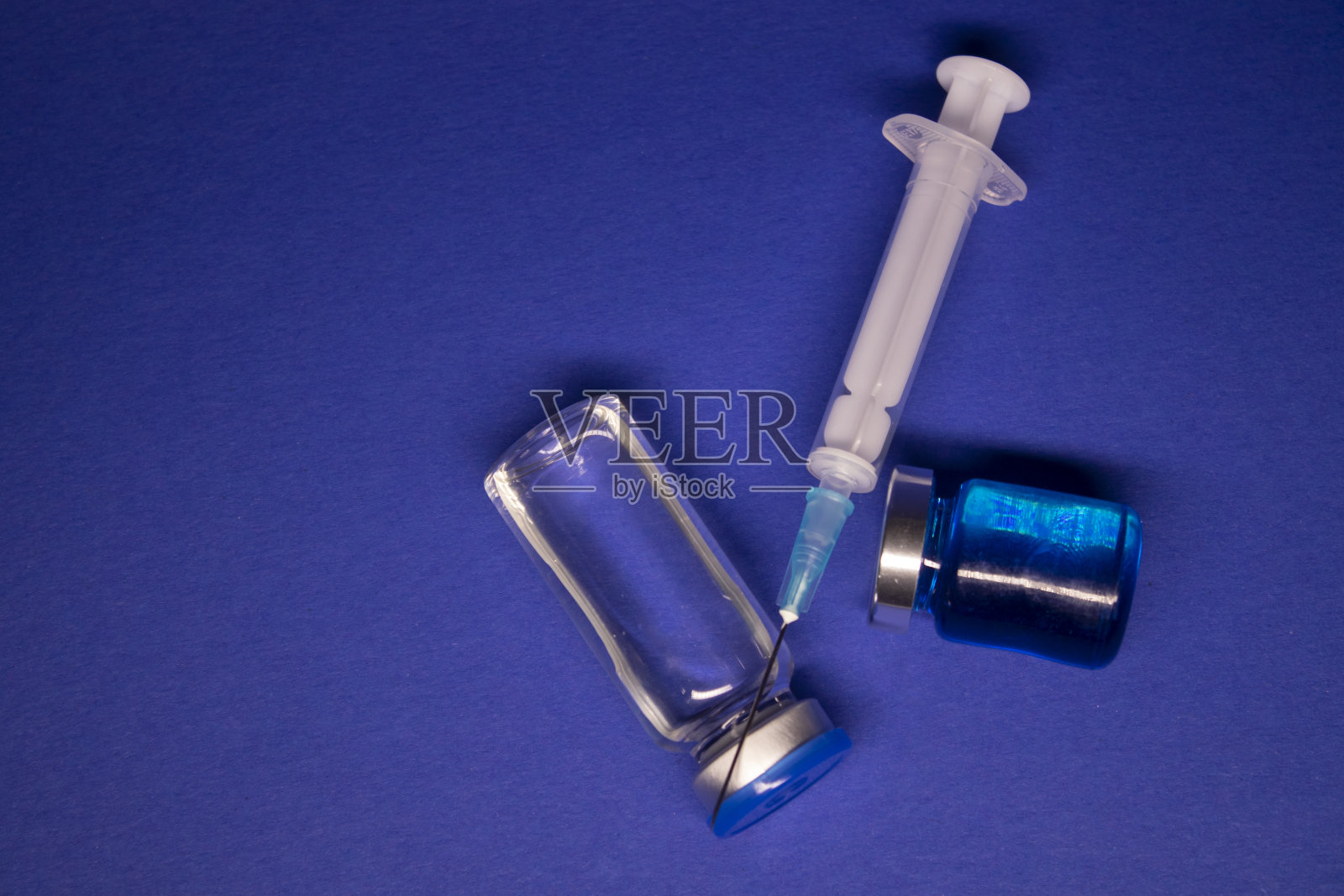 两个透明的无标签疫苗瓶,医用注射器注射针。孤立在蓝色背景。COVID-19冠状病毒疫苗的开发。治疗。世界研究竞赛照片摄影图片