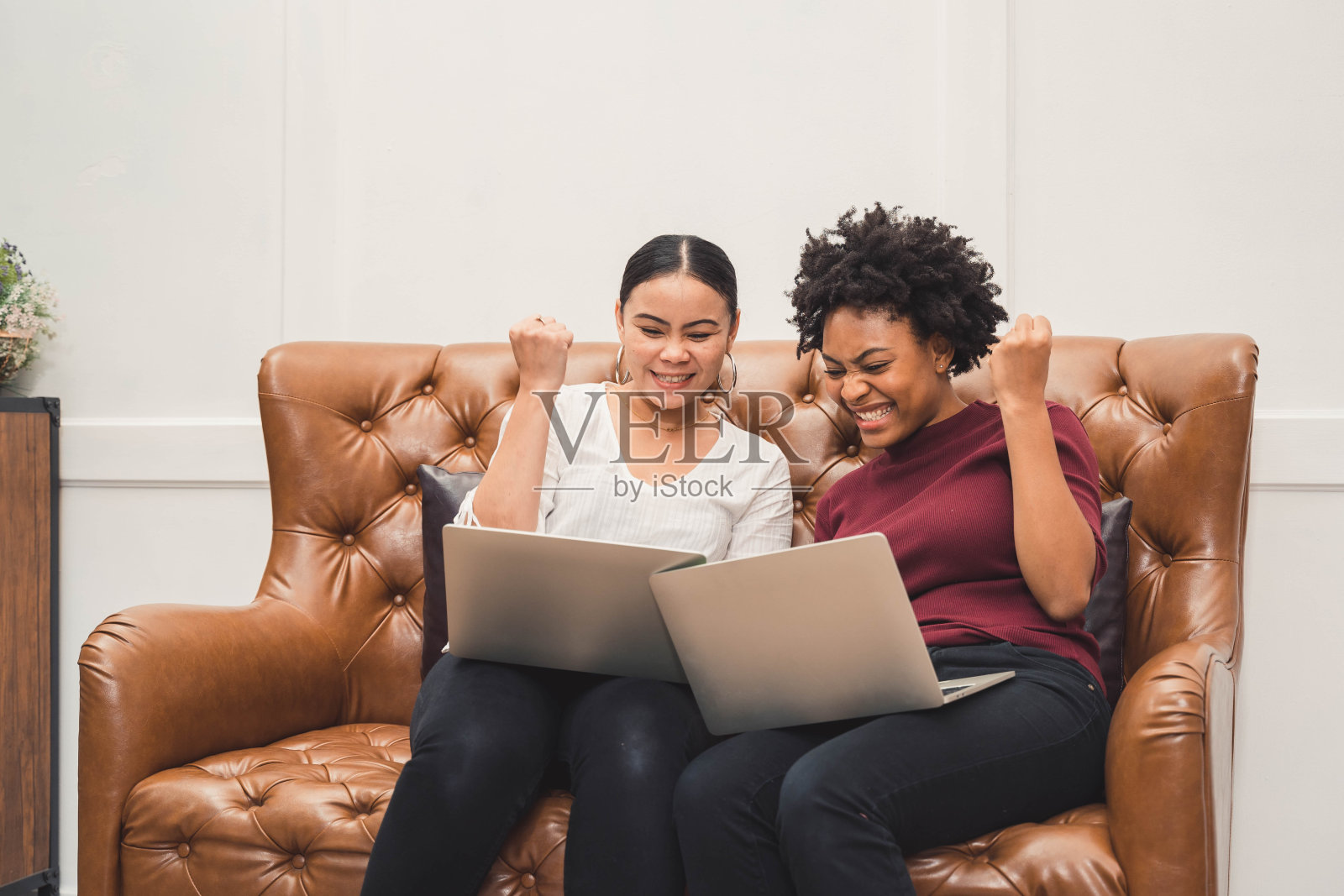 多文化的女性坐在沙发上用笔记本电脑,在客厅里放松,对着屏幕上的东西大笑照片摄影图片