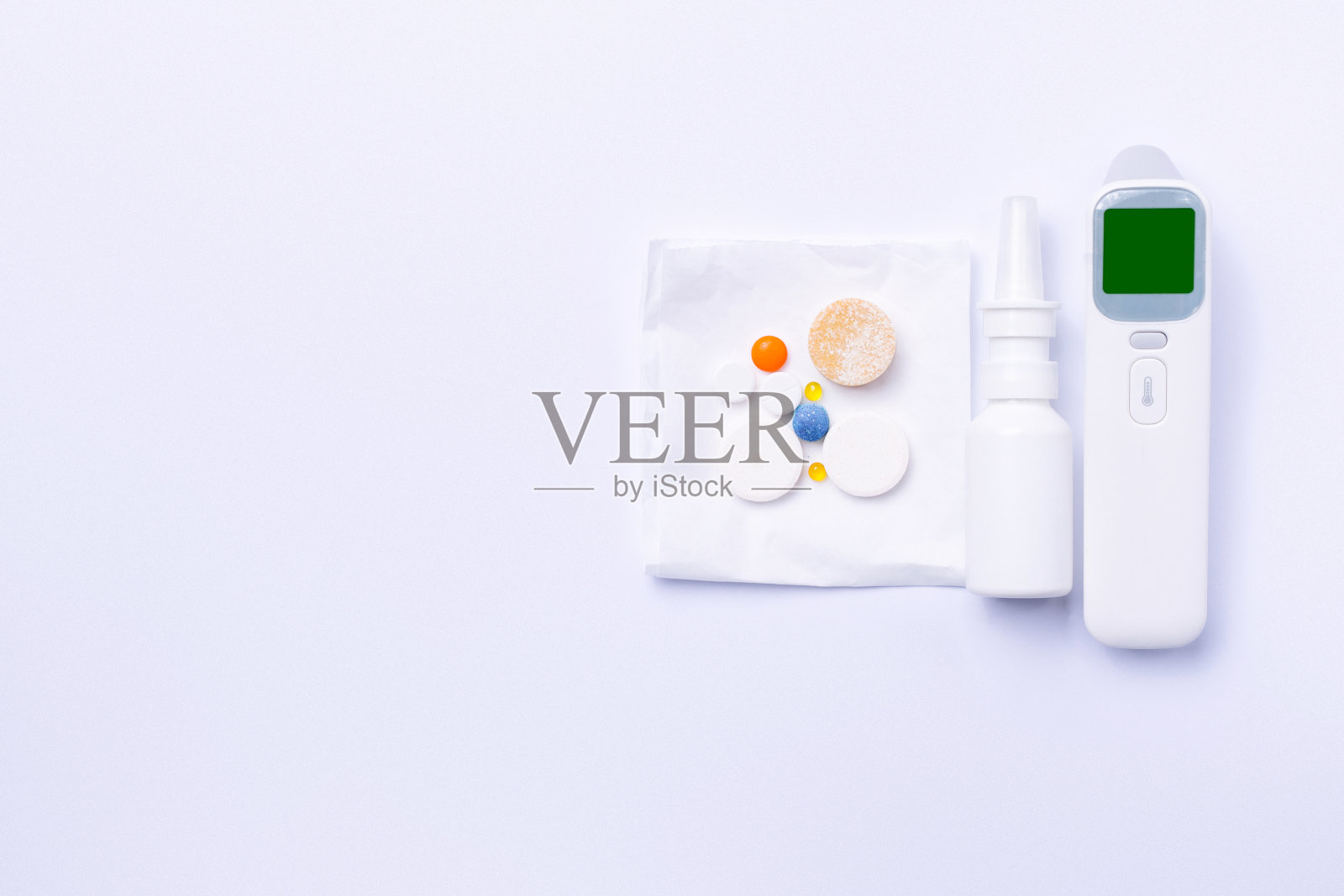 非接触式体温计,鼻喷剂和维生素。治疗感冒的重要药物。白色背景和侧面空白。照片摄影图片