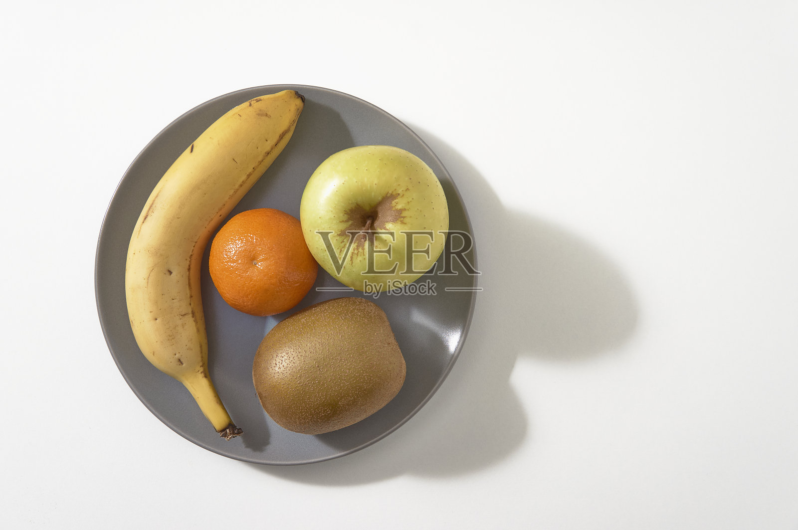 灰色的盘子上有各种水果,香蕉,橘子,苹果,猕猴桃在白色的背景。前视图。照片摄影图片