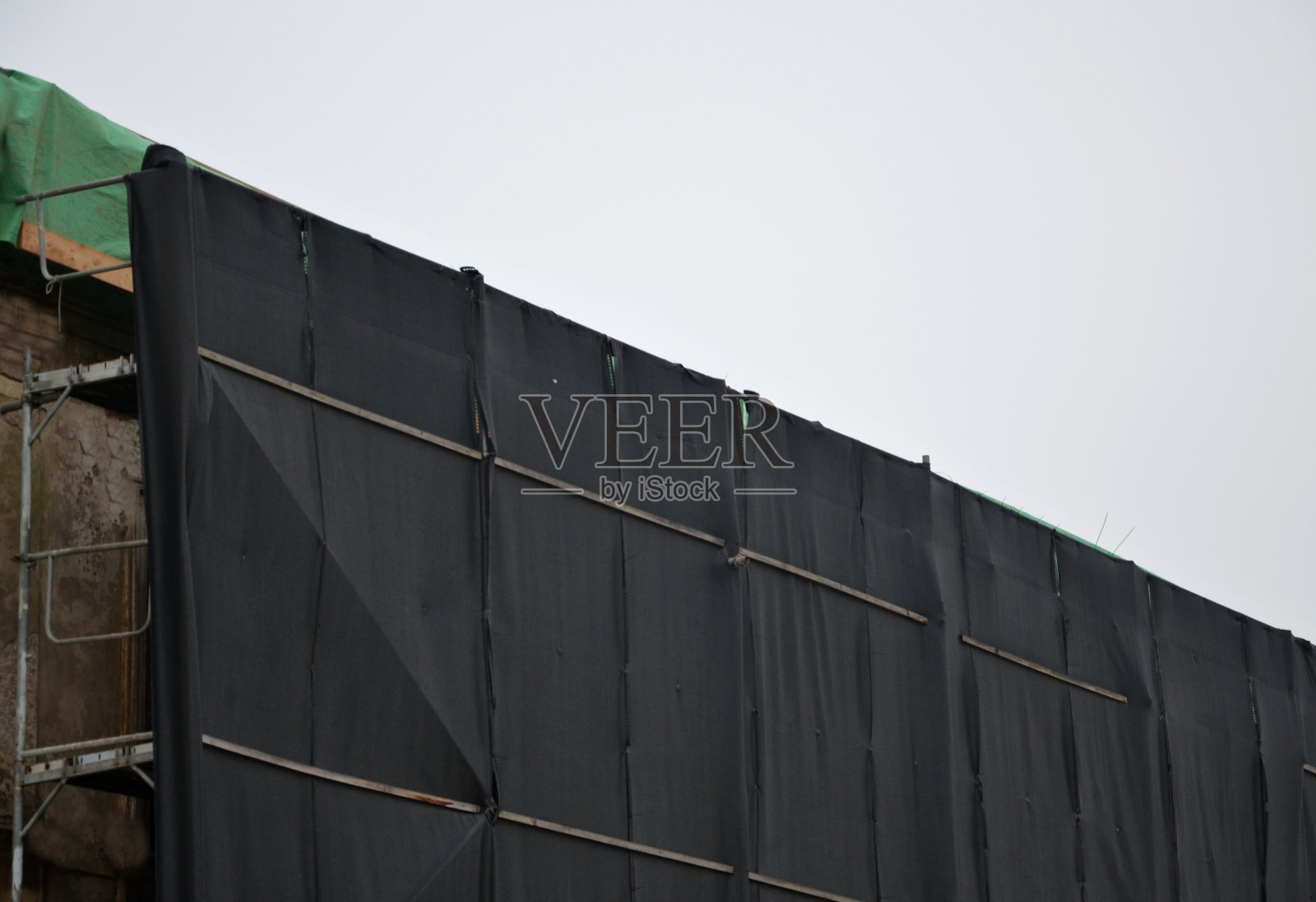 街上一所修理过的房子的脚手架。在人行道上覆盖着一个绿色的塑料布网,以防止跌落的物体和工具。防止行人和车辆受伤照片摄影图片