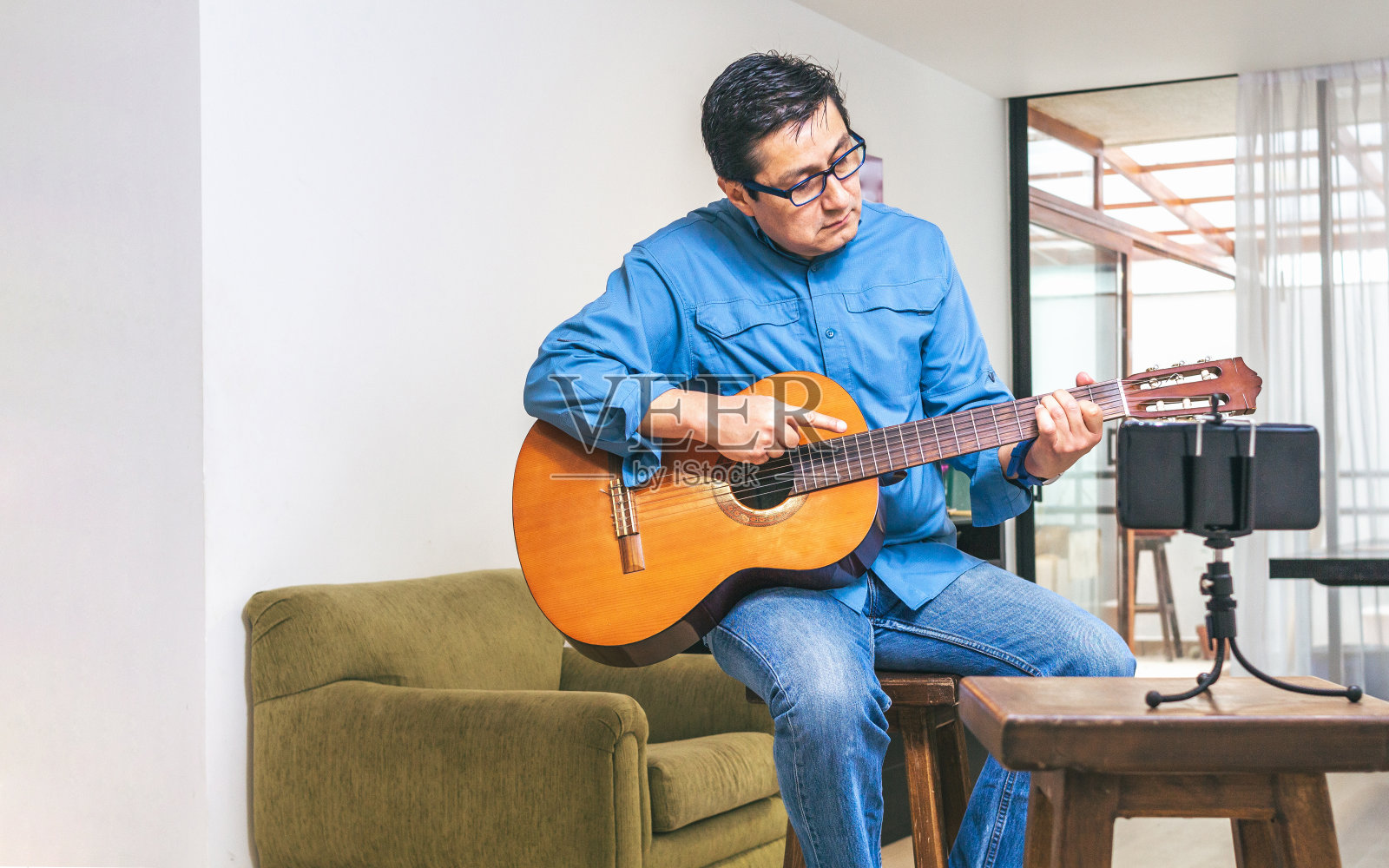 吉他老师坐在客厅的长椅上,用手机演奏和弦照片摄影图片