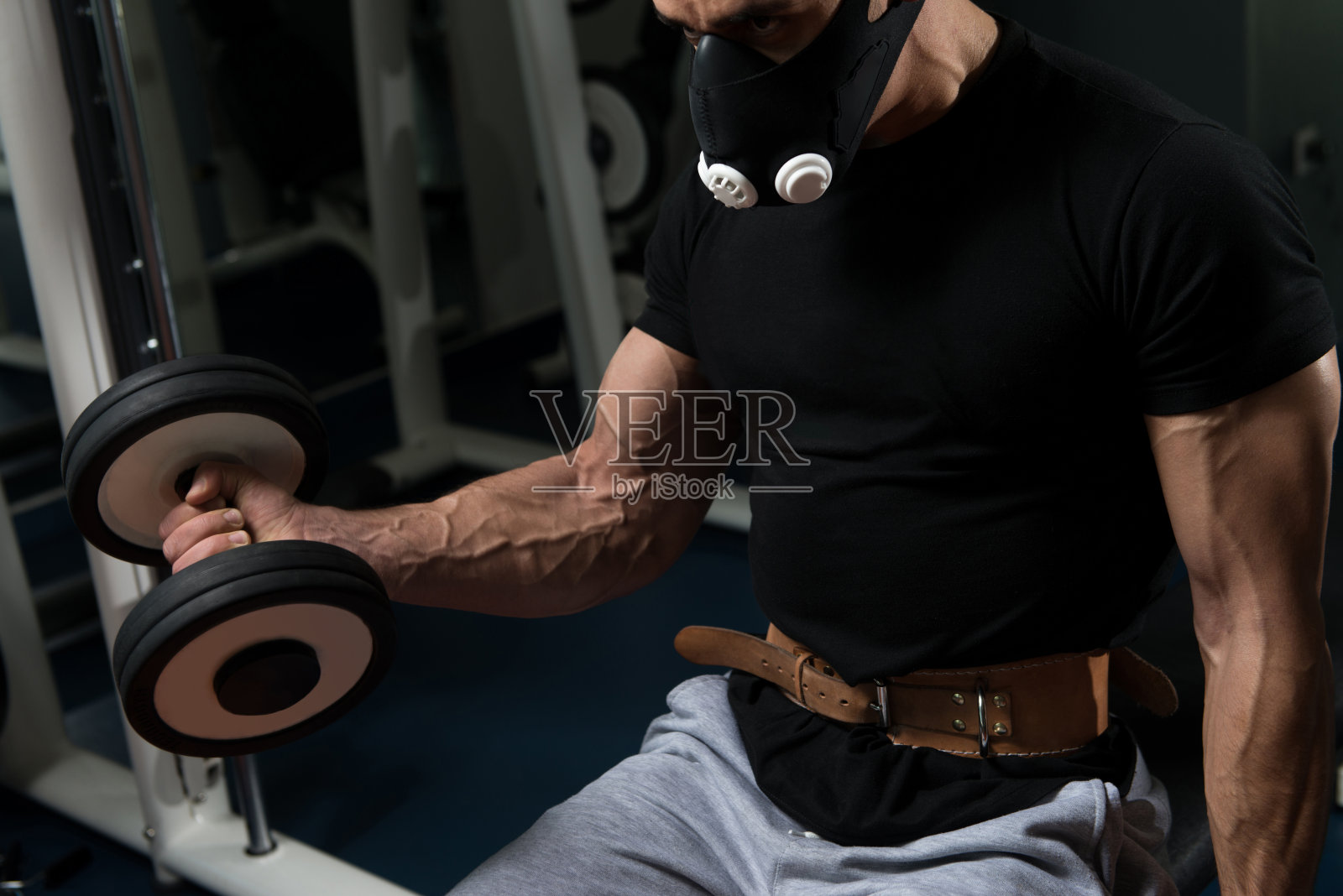 举着哑铃,戴着面罩锻炼二头肌的男人照片摄影图片