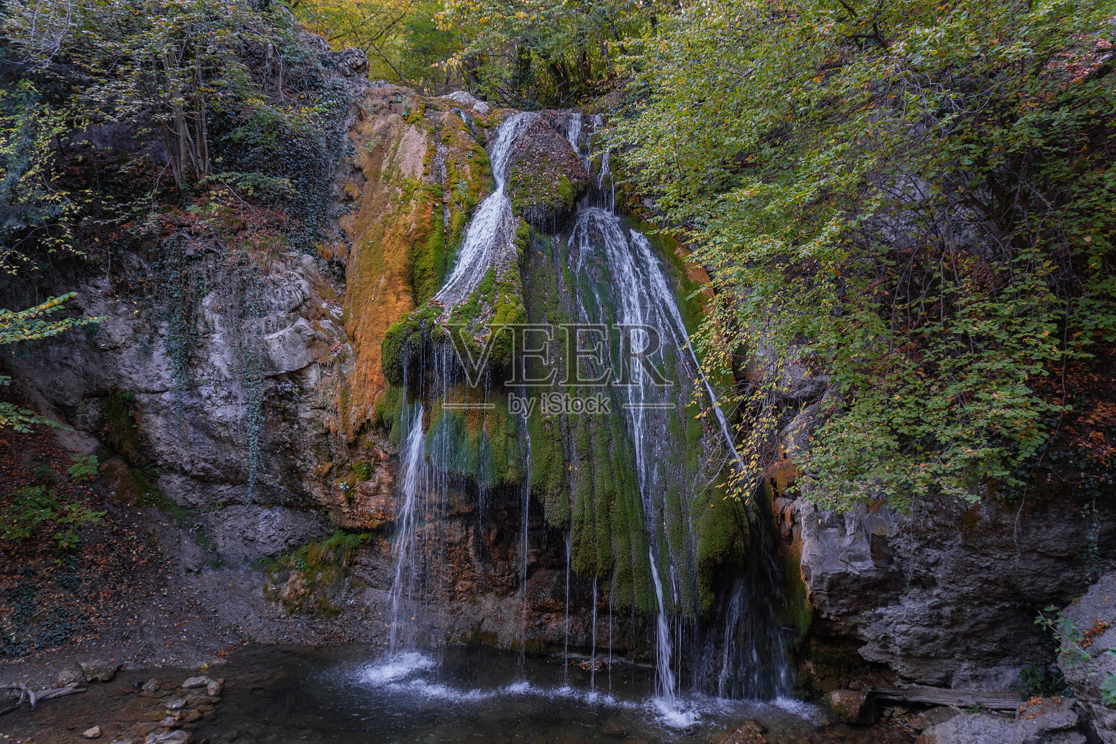 克里米亚的茱尔瀑布。溪水从覆盖着绿色和黄色苔藓的陡峭石壁上流下。水平的形象。照片摄影图片