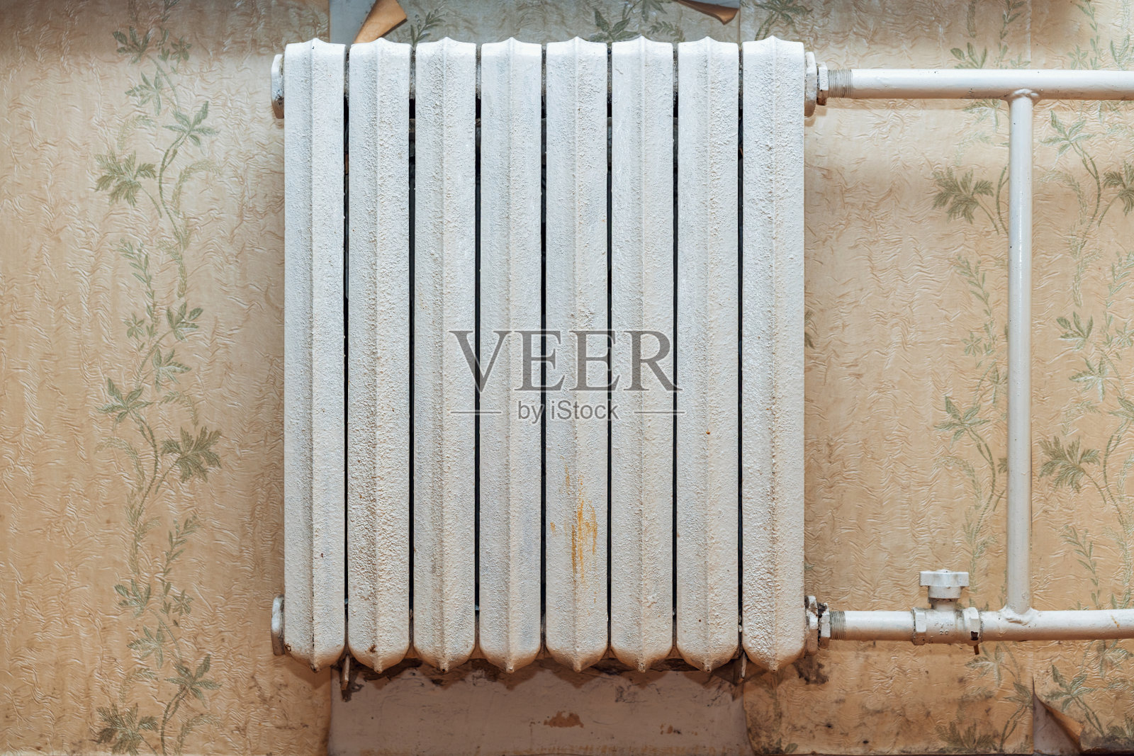 旧的铸铁电池挂在公寓楼的墙上,背景是老式的墙纸。照片摄影图片