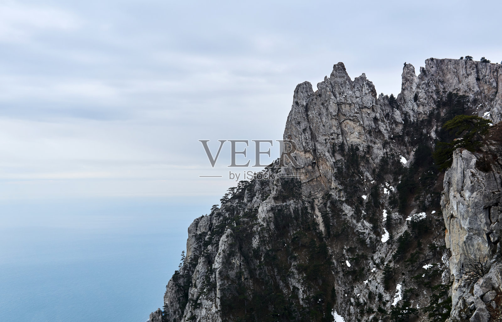 陡峭的悬崖上有稀疏的树木和冬季海面上的片片积雪照片摄影图片