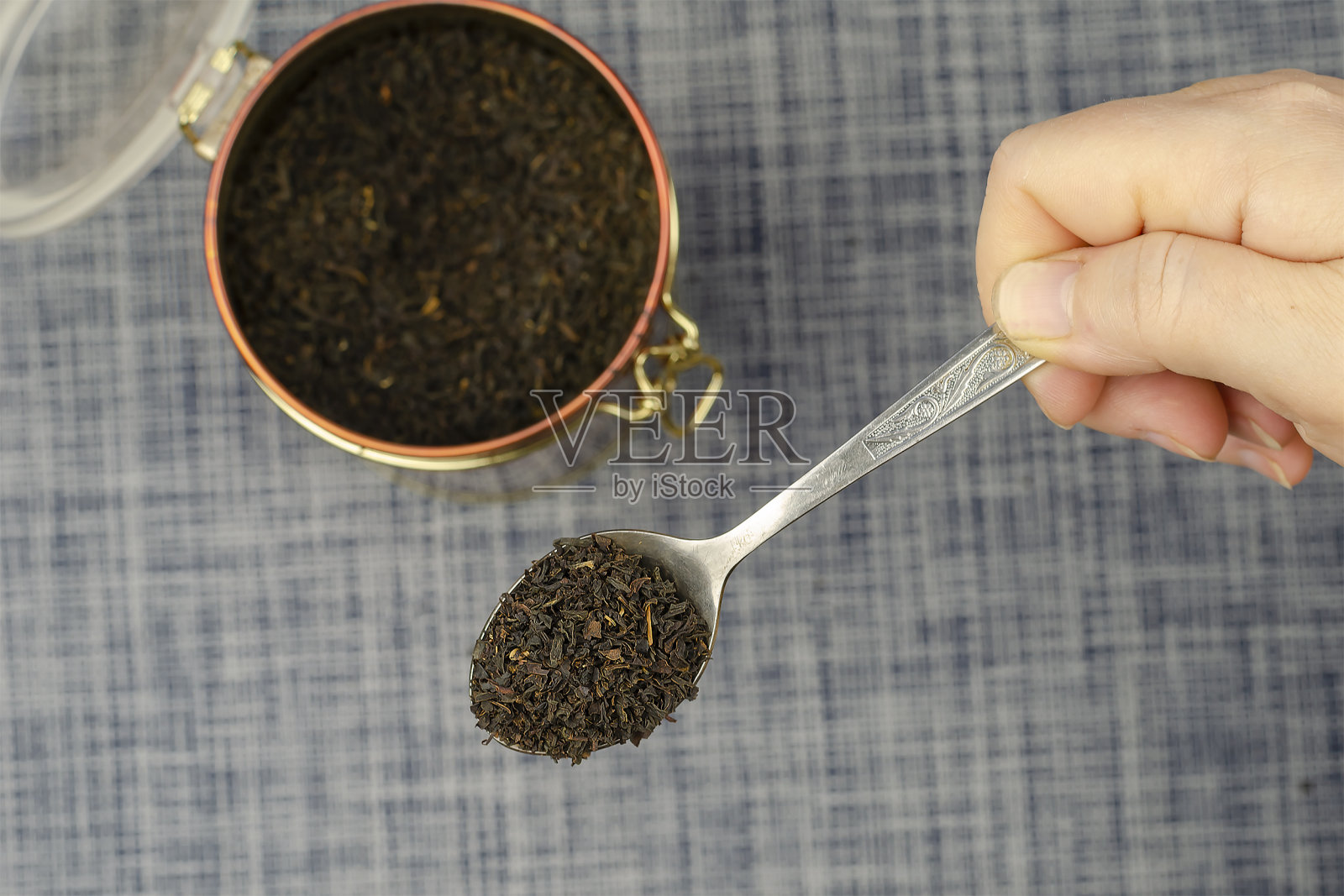 一个女人的手拿着一个金属勺子,里面放着干茶叶。照片摄影图片