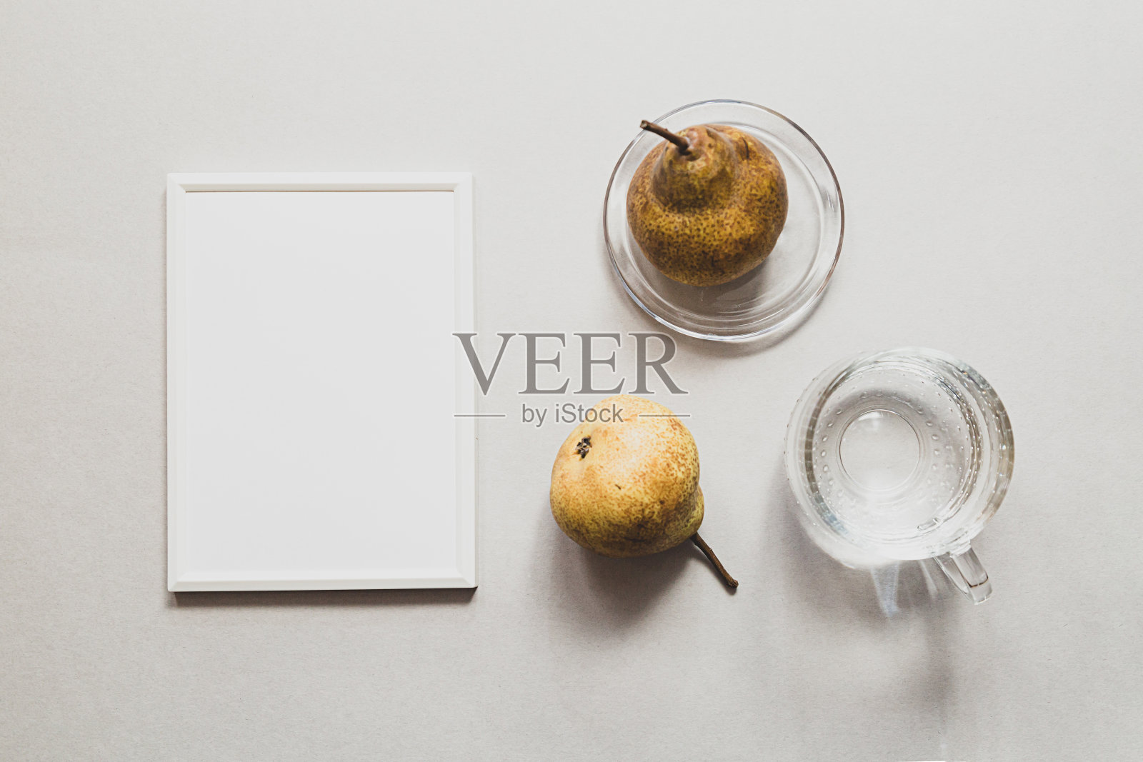 现代静物与白色空相框。夏日作文用梨和一杯水。模拟平躺在灯光背景上照片摄影图片