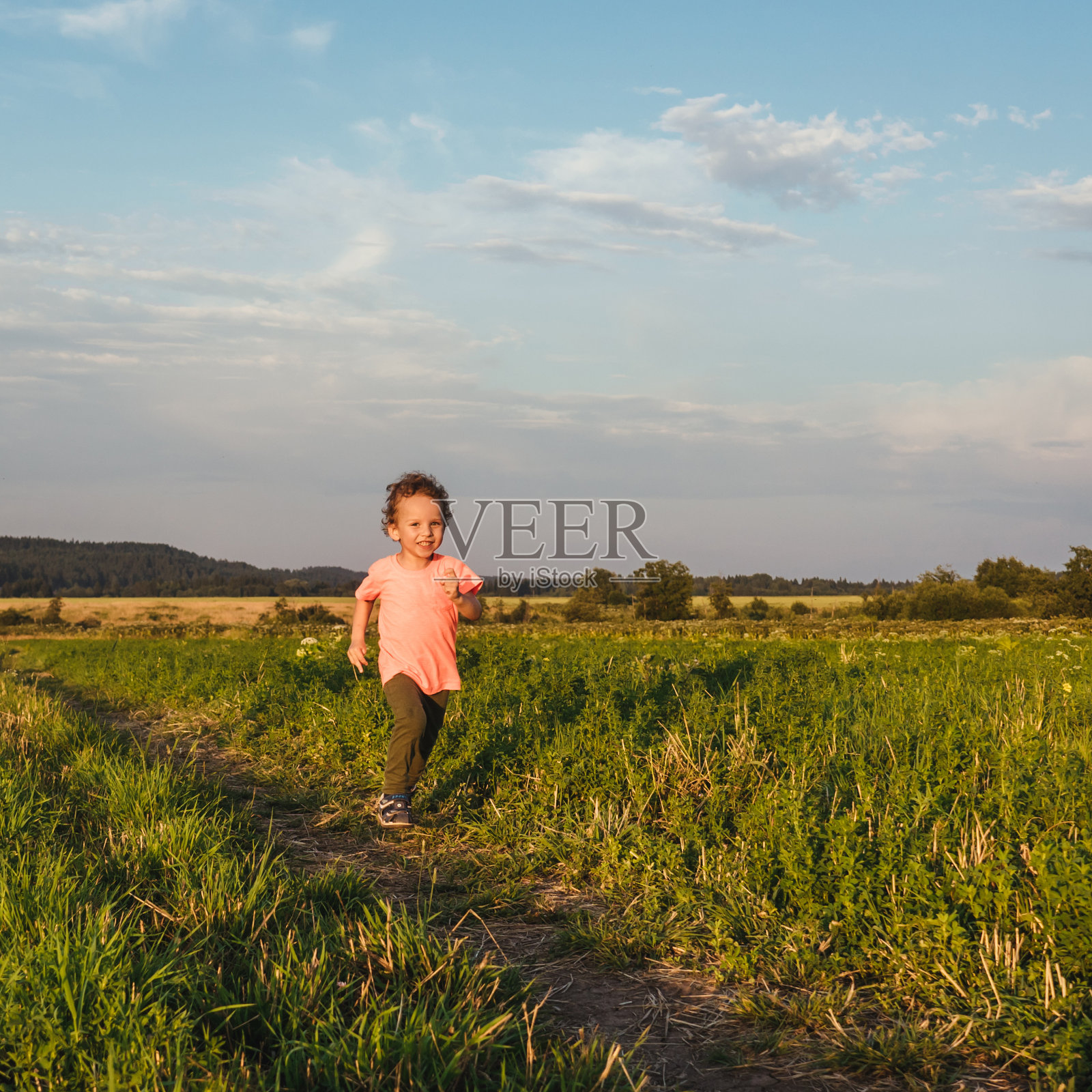 夕阳下,小男孩在草地上奔跑。照片摄影图片