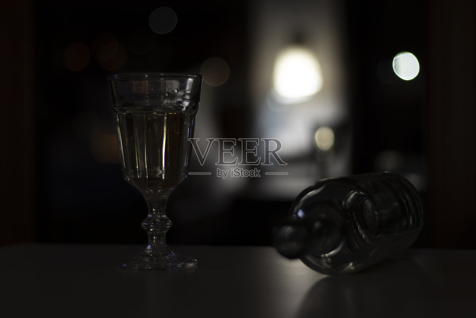 黑暗的房间里,桌子上放着一杯酒和一个空瓶子。照片摄影图片