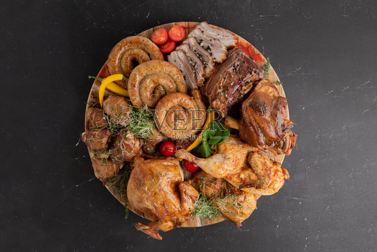 一个大的肉盘。熏猪肉香肠,烤鸡,牛肉,猪肉,放在一个大盘子上,背景是黑色的照片摄影图片