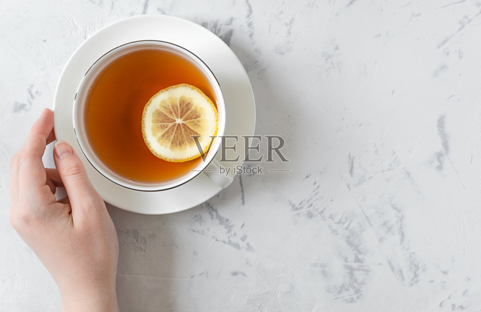 灰色的桌子上放着白色的柠檬茶和手持的杯子。照片摄影图片