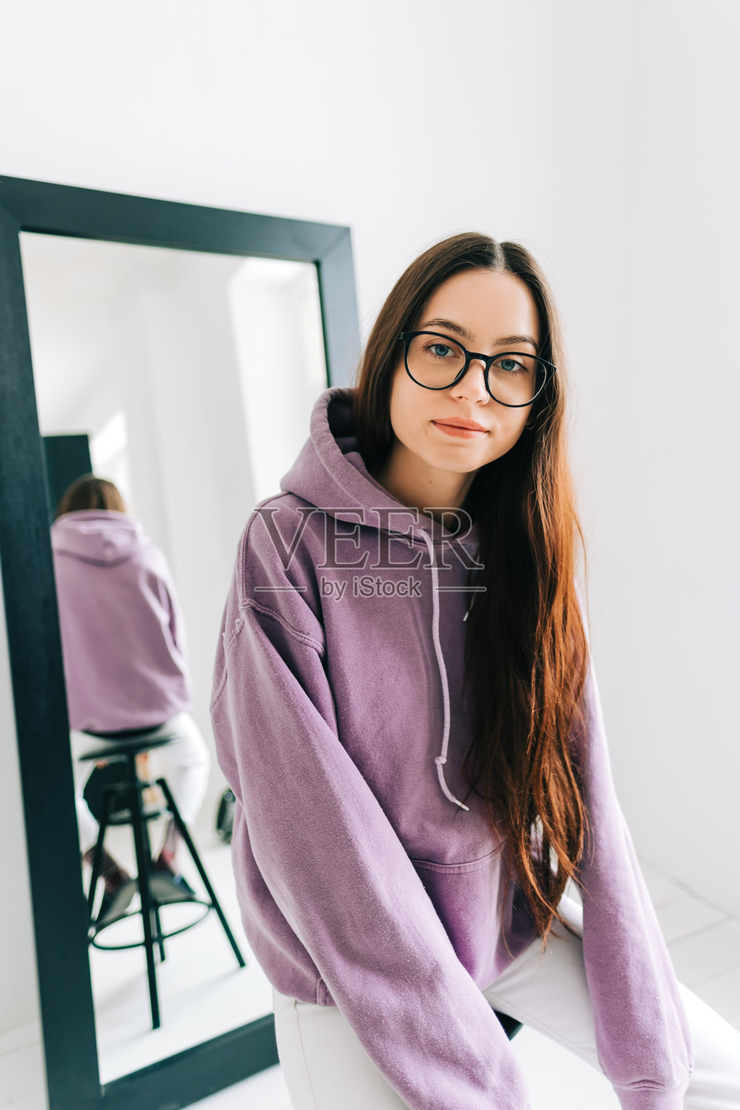 在阳光明媚的日子里,漂亮的年轻白人妇女在客厅的镜子里戴眼镜的肖像。照片摄影图片