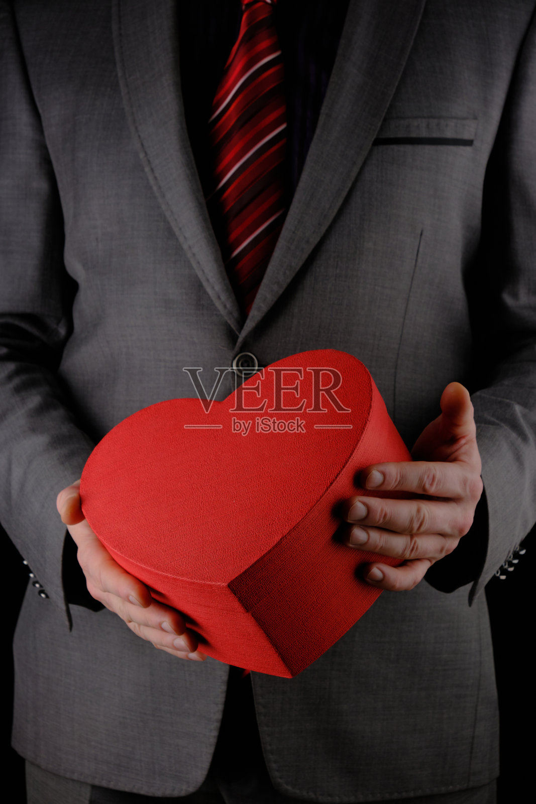 不认识的西装男子拿着心形礼物红盒子,祝贺概念,黑色背景照片摄影图片