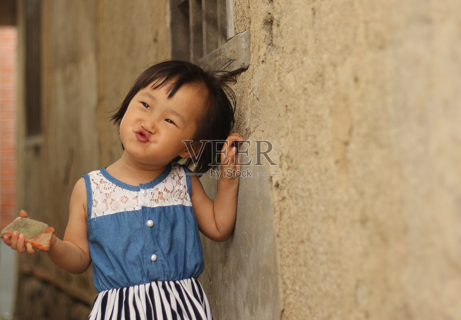 一个亚洲女孩在一堵斑驳的旧墙前演奏。照片摄影图片