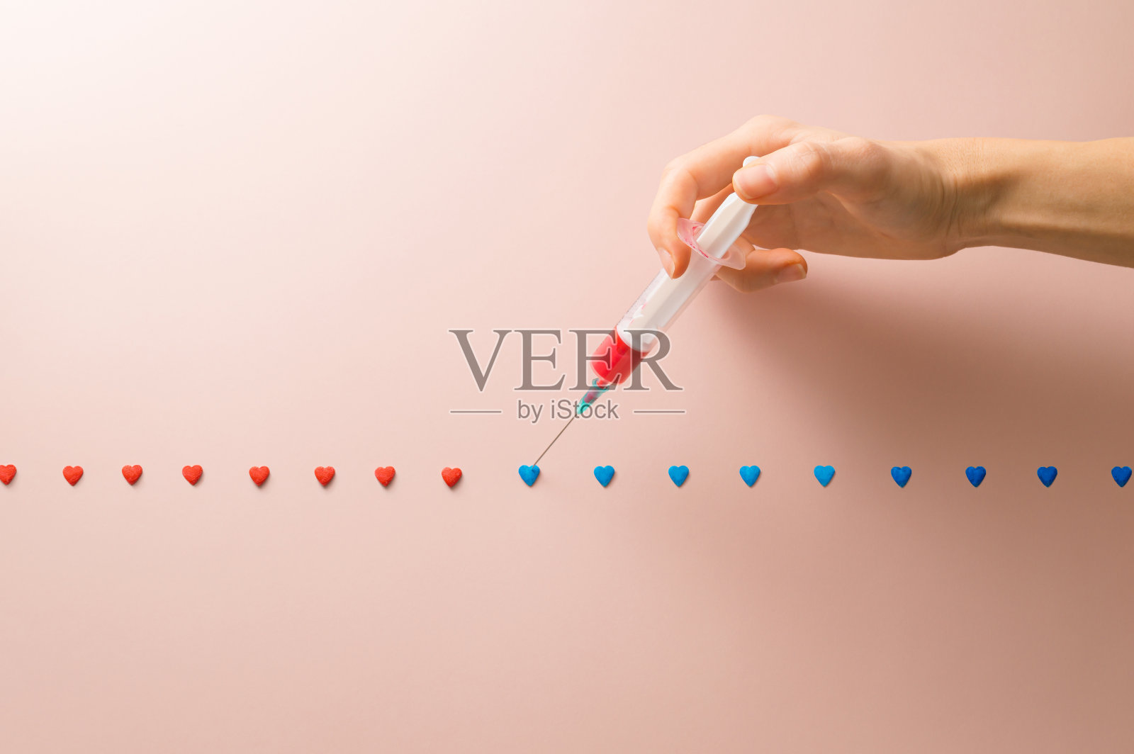 用注射器把蓝色的心涂成红色。创造性的艺术概念。照片摄影图片