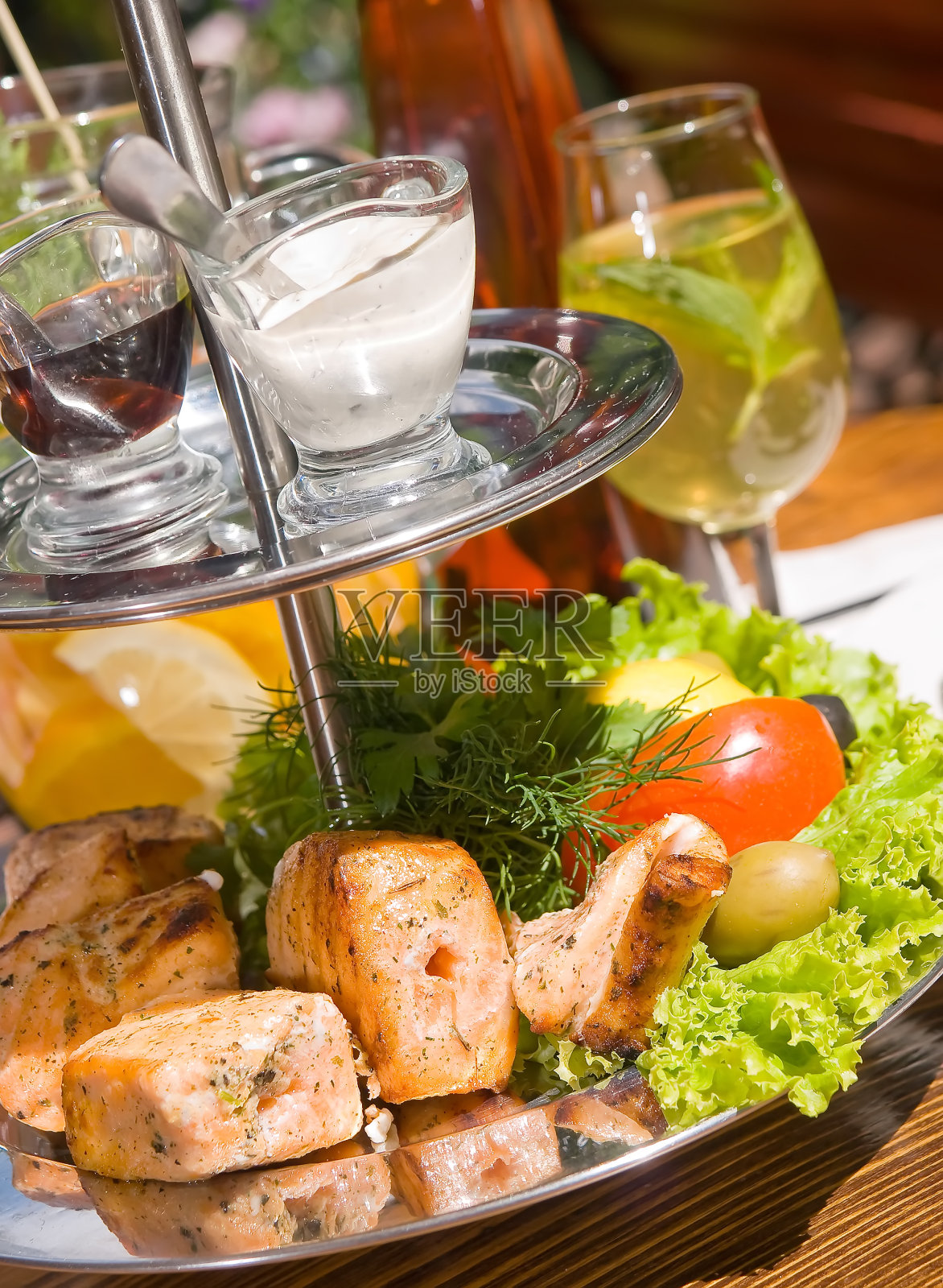 在一个阳光明媚的日子,午餐供应在夏季餐厅露台。一份烤鲑鱼片配酱汁和新鲜蔬菜茄子,番茄和香草酱。垂直图照片摄影图片