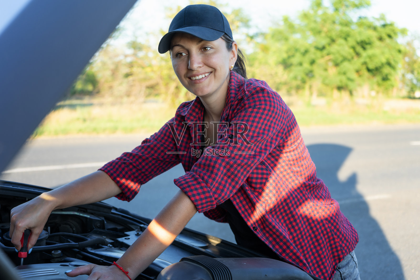 漂亮的年轻女子在路边修车。女孩穿着衬衫和牛仔裤准备修理她的车。女人机械。路上的破车和等待帮助的女人照片摄影图片