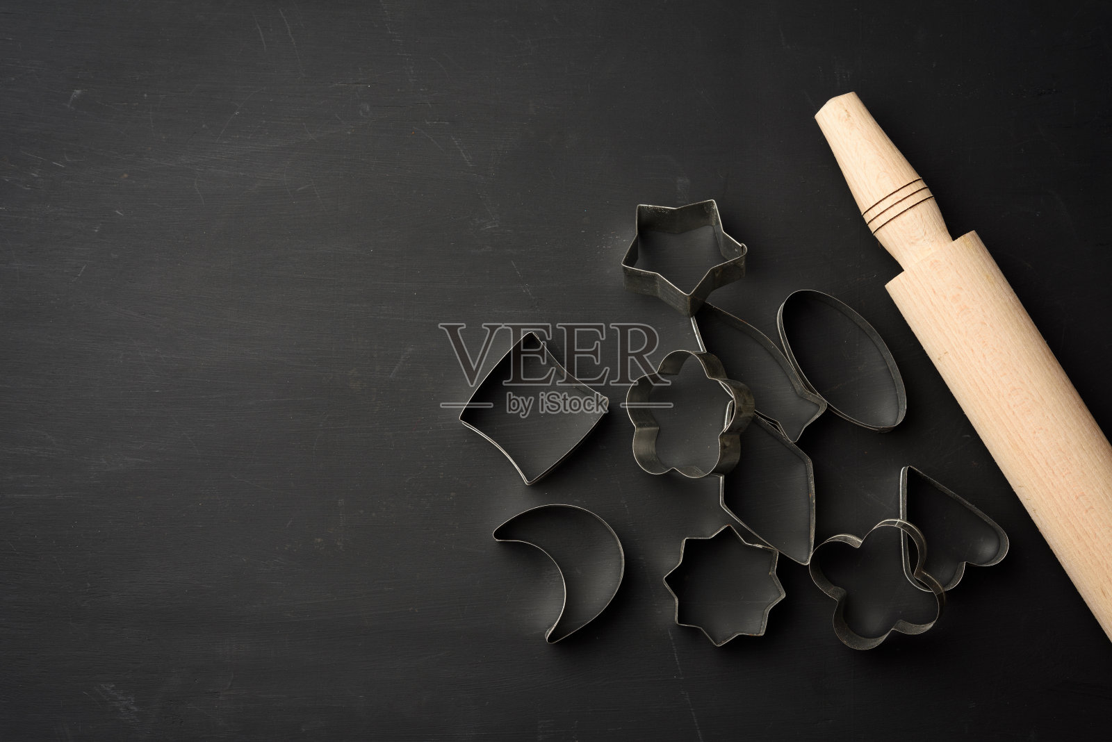 黑色背景上的金属饼干切割机和木制擀面杖照片摄影图片