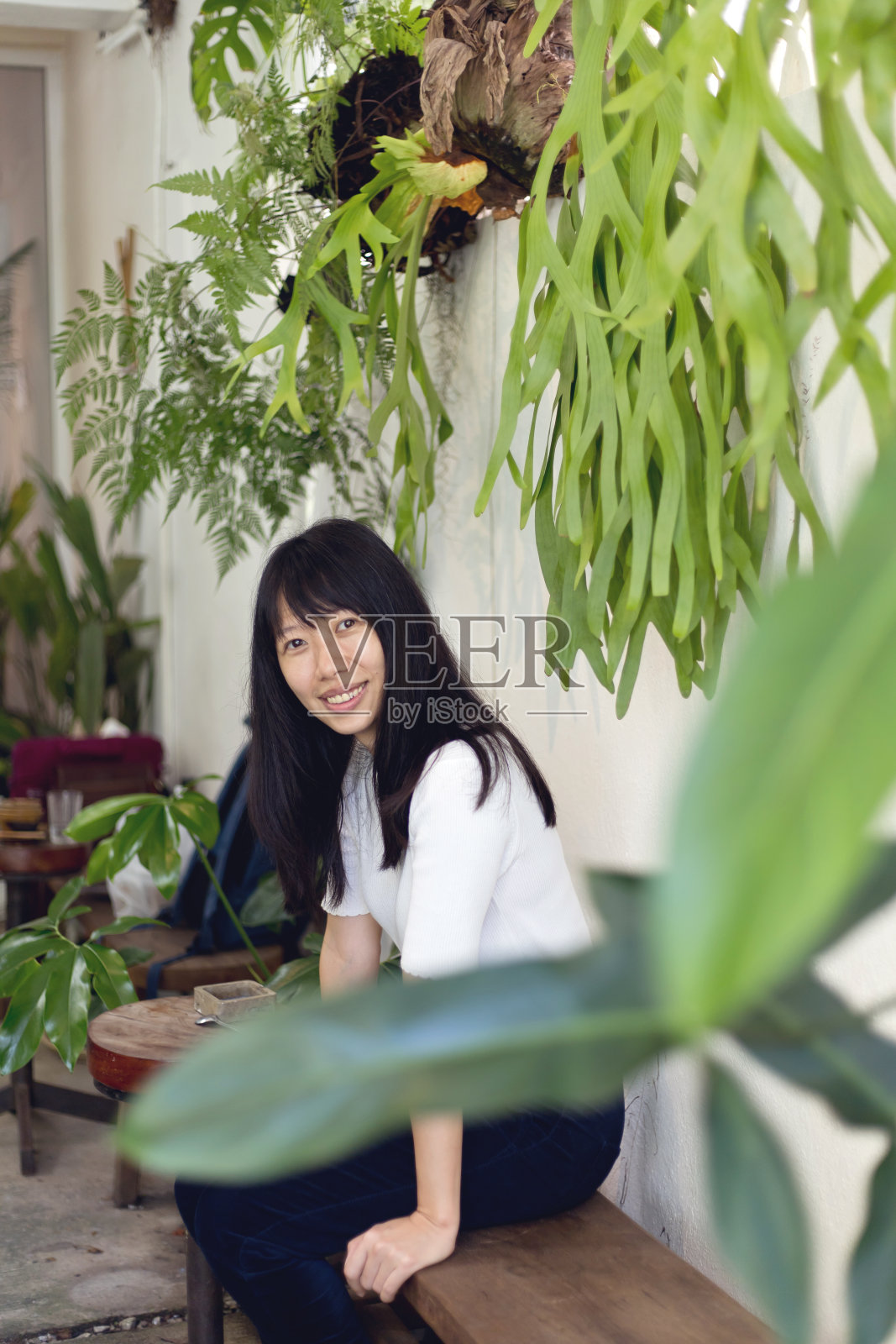 年轻的亚洲女人坐在和微笑在一个美丽的绿色植物的户外咖啡馆照片摄影图片