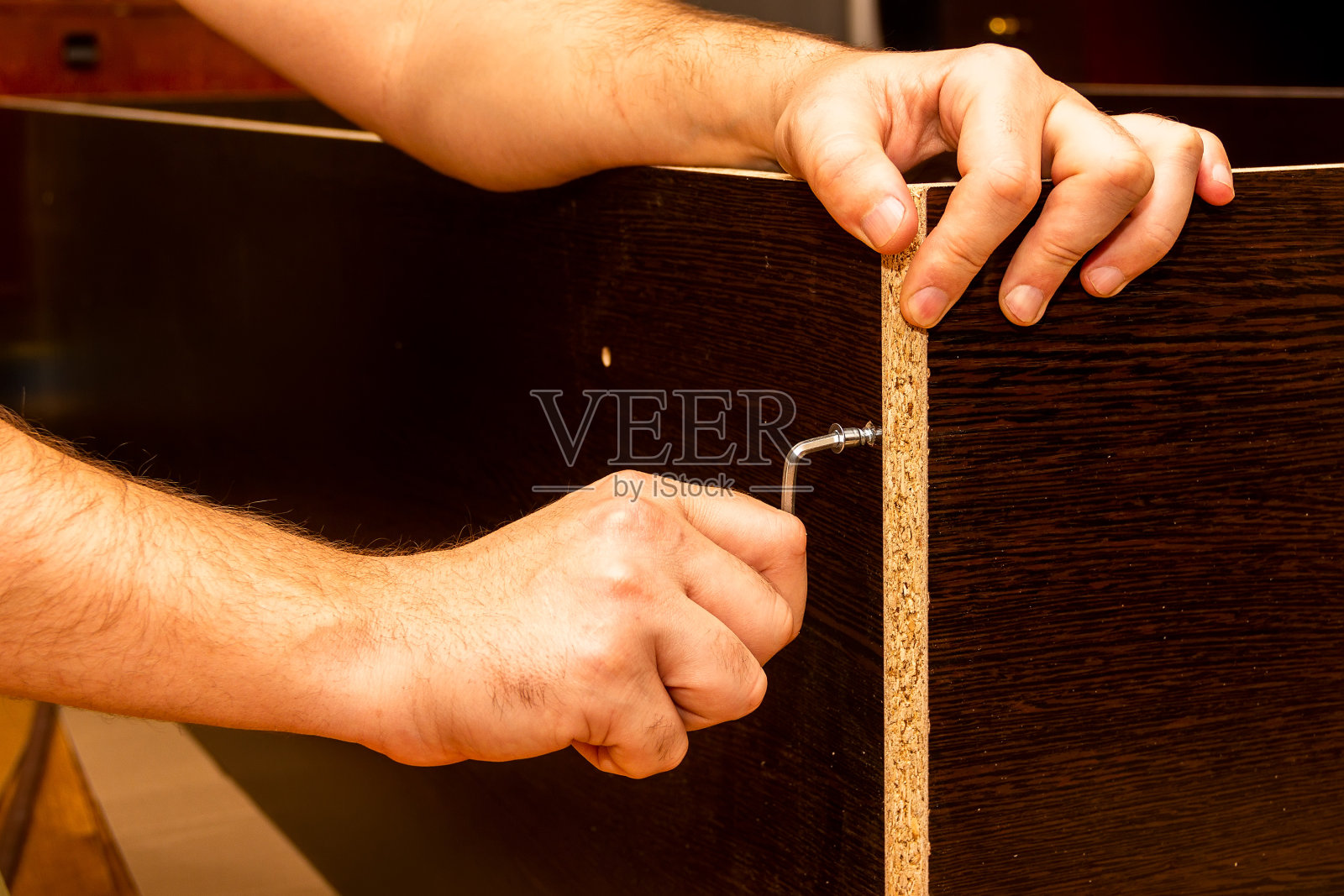 男人的手组装家具与六角键制成的深棕色层压刨花板照片摄影图片