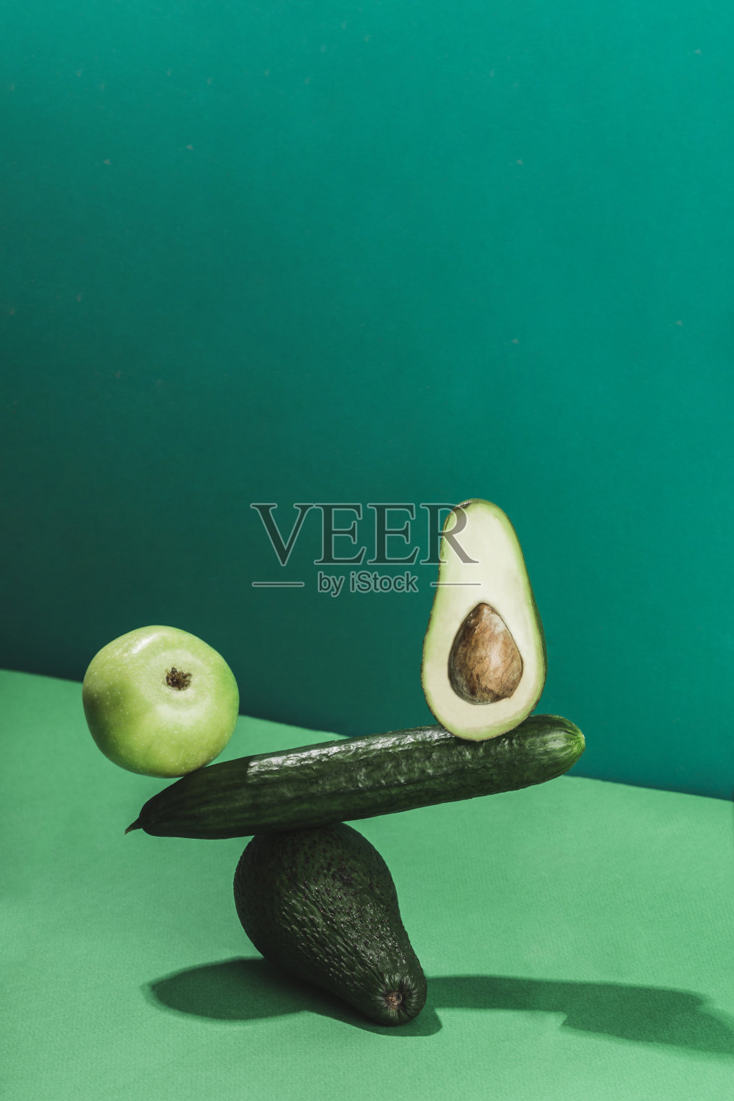 平衡新鲜蔬菜和水果的概念,黄瓜,鳄梨和在绿色背景下的苹果。照片摄影图片